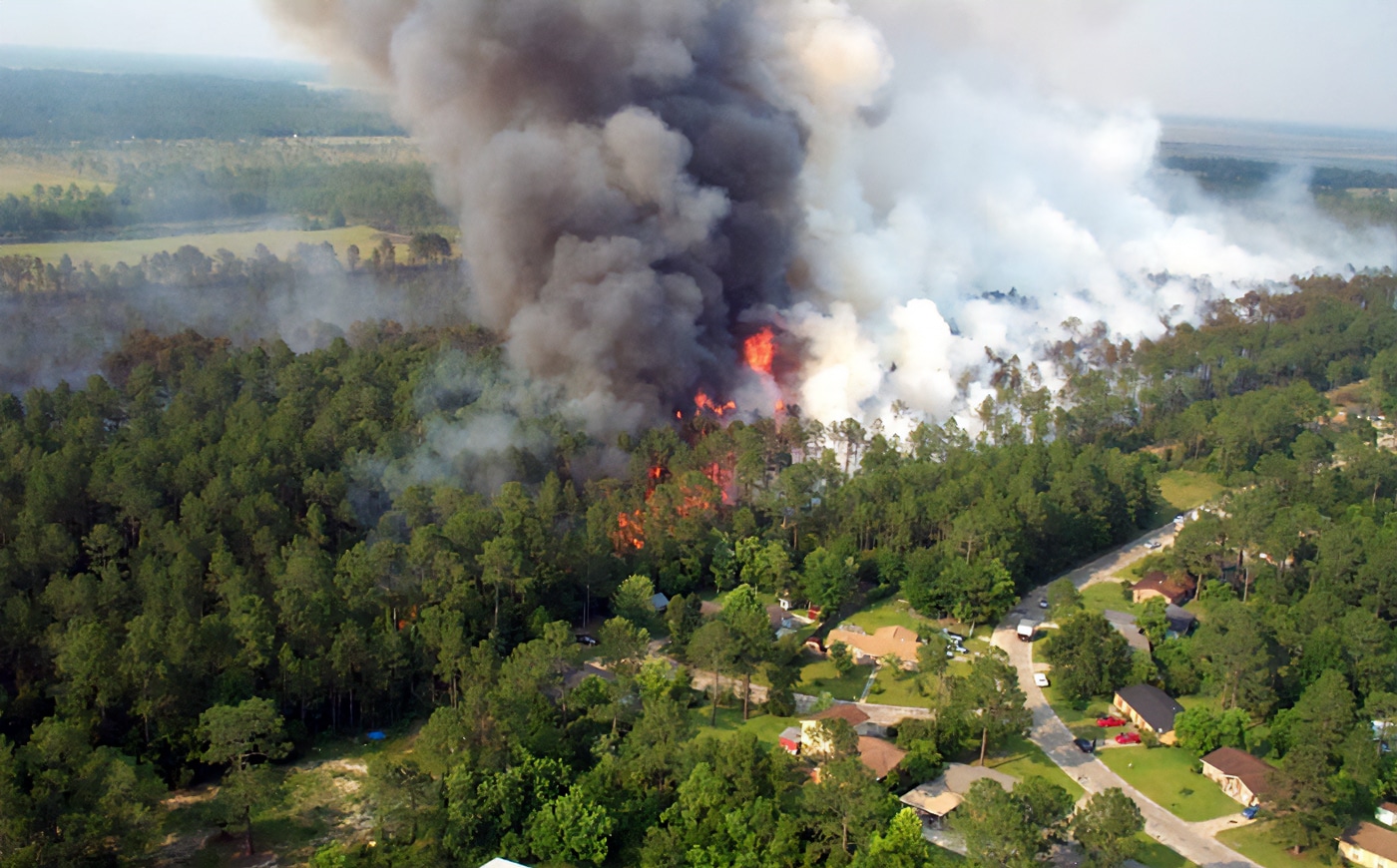 In this photograph we see a raging forest fire and smoke approaching a subdivision in a suburban community.