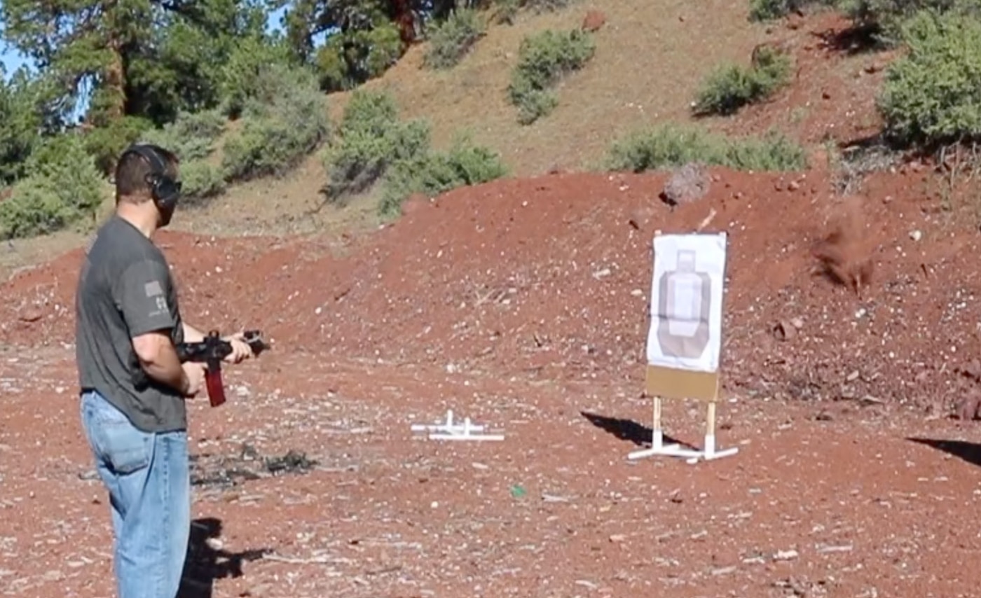 The author demonstrating hip-level shooting position with an AR pistol, holding the firearm at waist height while the Viridian X5L laser provides an aiming point. The Viridian X5L review covers unconventional shooting techniques. Light and laser unit capabilities support compressed firing positions. Green lasers enable shooting without traditional sight alignment. Non-standard response drills prepare for imperfect scenarios. The X5L provides aiming reference at any height. Close-quarters engagements may prevent shouldering firearms. Combined units expand tactical options under stress. Defensive training must address realistic limitations.