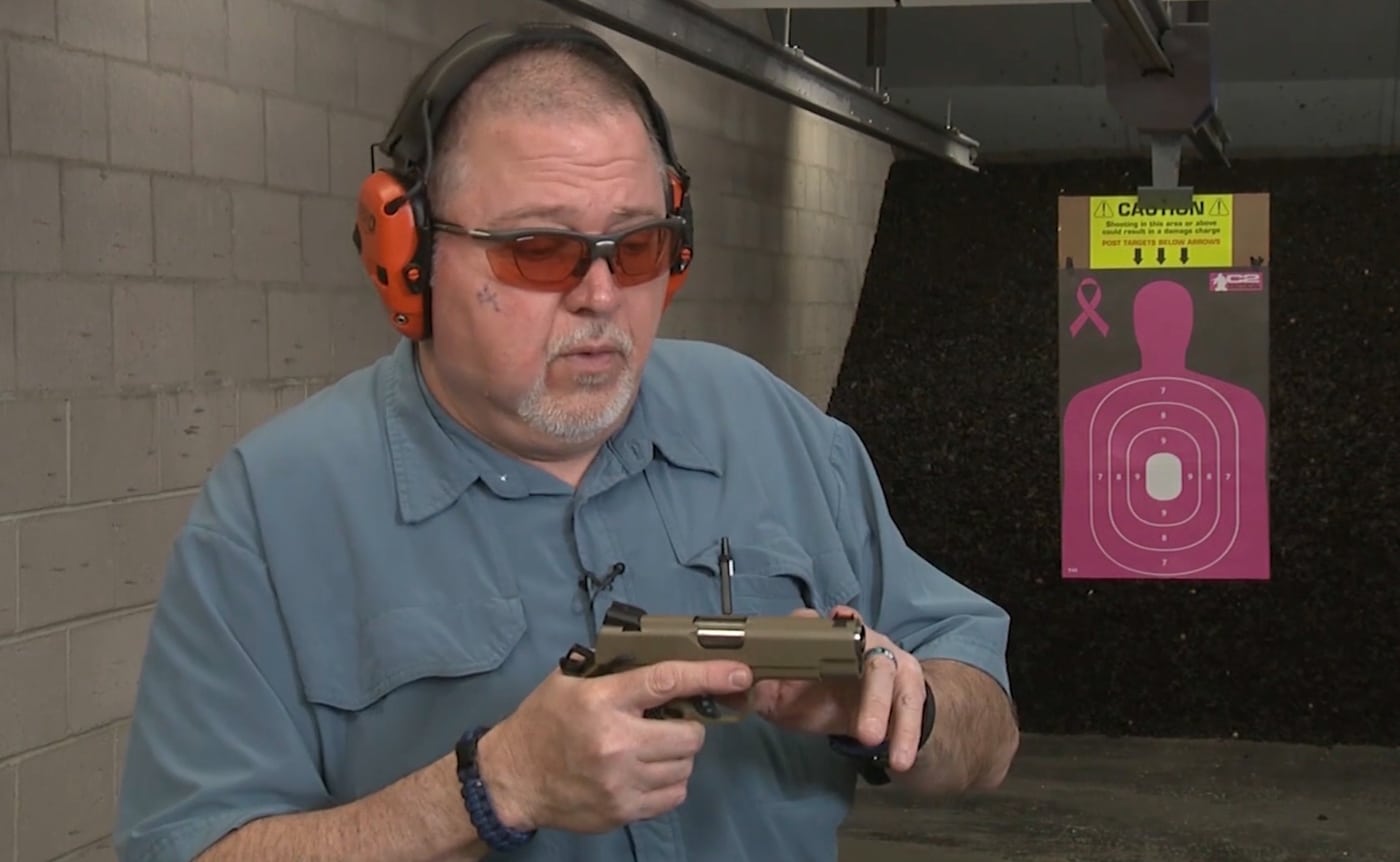 The author's finger points to the bright fiber optic front sight on the EMP4's slide, showing the highly visible aiming point that contrasts sharply against the pistol's finish and surrounding environment. The EMP4 features factory fiber optic front sight. Springfield Armory EMP4 provides quick sight acquisition capability. Compact 1911 pistols benefit from high-visibility sight systems. The EMP4 includes low-mount rear sight with white dots. Fiber optic sights excel in varied lighting conditions. Springfield's compact pistol comes well-equipped from factory. The EMP4 delivers clean, intuitive sight picture alignment.