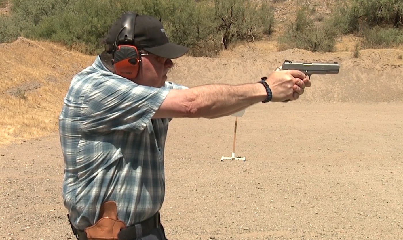 A shooter extends a pistol directly toward a target with arms fully extended, sights aligned, and trigger finger indexed on the trigger face. Pistol presentation completes with full extension. Drawing a handgun from a holster finishes at shooting position. Proper firearm alignment enables accurate engagement. Handgun deployment achieves sight-target-eye relationship. Defensive pistol techniques emphasize straight extension paths. Combat shooting mechanics eliminate curved motion patterns. Holster-to-target sequence concludes with ready position. Tactical handgun presentation reaches firing configuration.