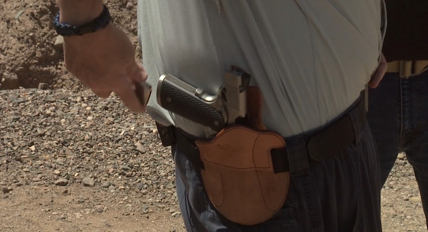 A shooter carefully inserting a pistol into a belt-mounted holster during a one-handed reload drill at the shooting range. One handed malfunction clearance uses holster retention strategically. Clearing pistol jam with one hand requires stable gun placement. Reholstering provides hands-free pistol security. Belt holsters offer reliable firearm retention. Single-hand techniques eliminate juggling risks. Defensive shooters utilize equipment purposefully. Holster-based reloads maintain weapon control. Practical training addresses real-world constraints.