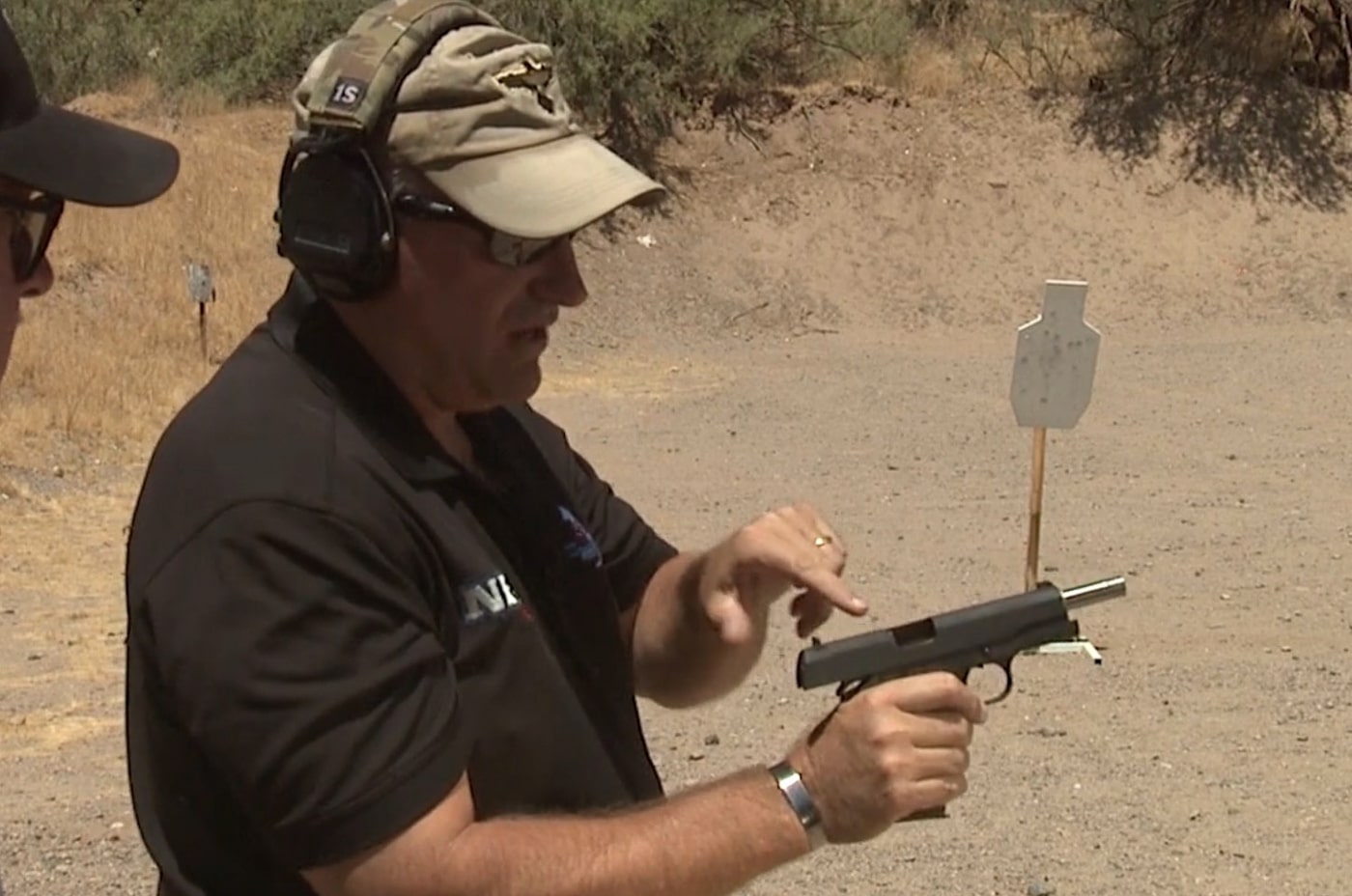 An instructor pointing to the ejection port and chamber area of a 1911 pistol while explaining malfunction points to a student. One handed malfunction clearance begins with understanding failure types. Clearing pistol jam with one hand requires diagnostic knowledge. 1911 pistols experience specific stoppage patterns. Ejection port obstructions cause common malfunctions. Feed ramp issues create ammunition failures. Instructors demonstrate mechanical problem areas. Pistol education improves troubleshooting speed. Firearm reliability depends on recognizing failure signs.