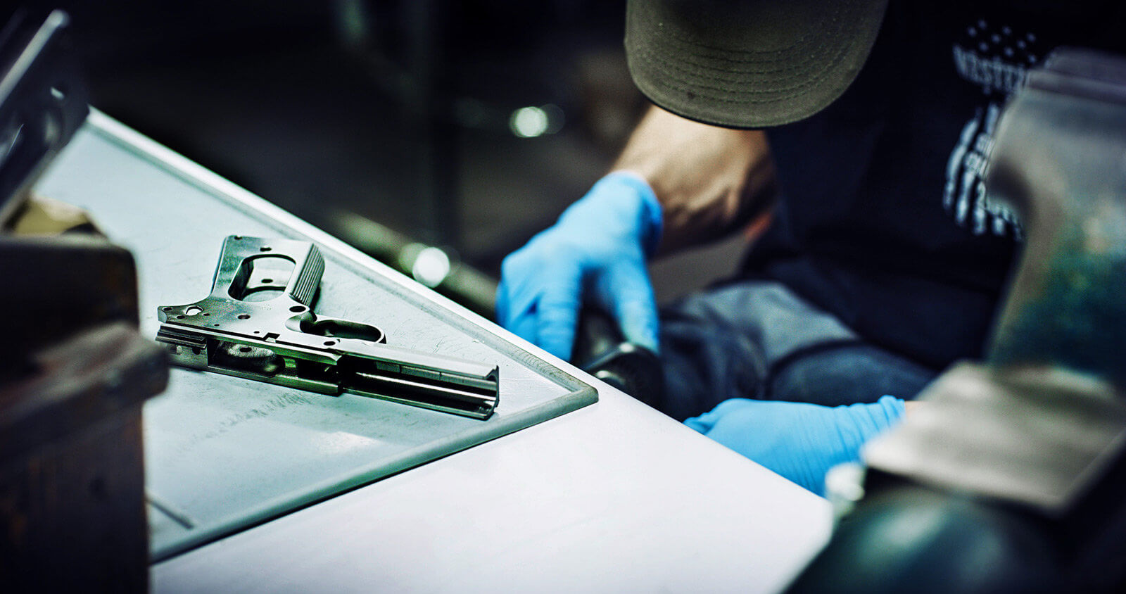 In this photo, a gunsmith has a disassembled 1911 handgun on his workbench. He is getting ready to swap the mainspring housing, upgrade the grips safety, add a new rear sight, install an extended beavertail, swap out the barrel bushing, install a full-length guide rod, update the sear and install a new extractor. For 1911 guys, a checker grip is likely better than a Hogue option, and a new recoil spring might be a good upgrade as well.