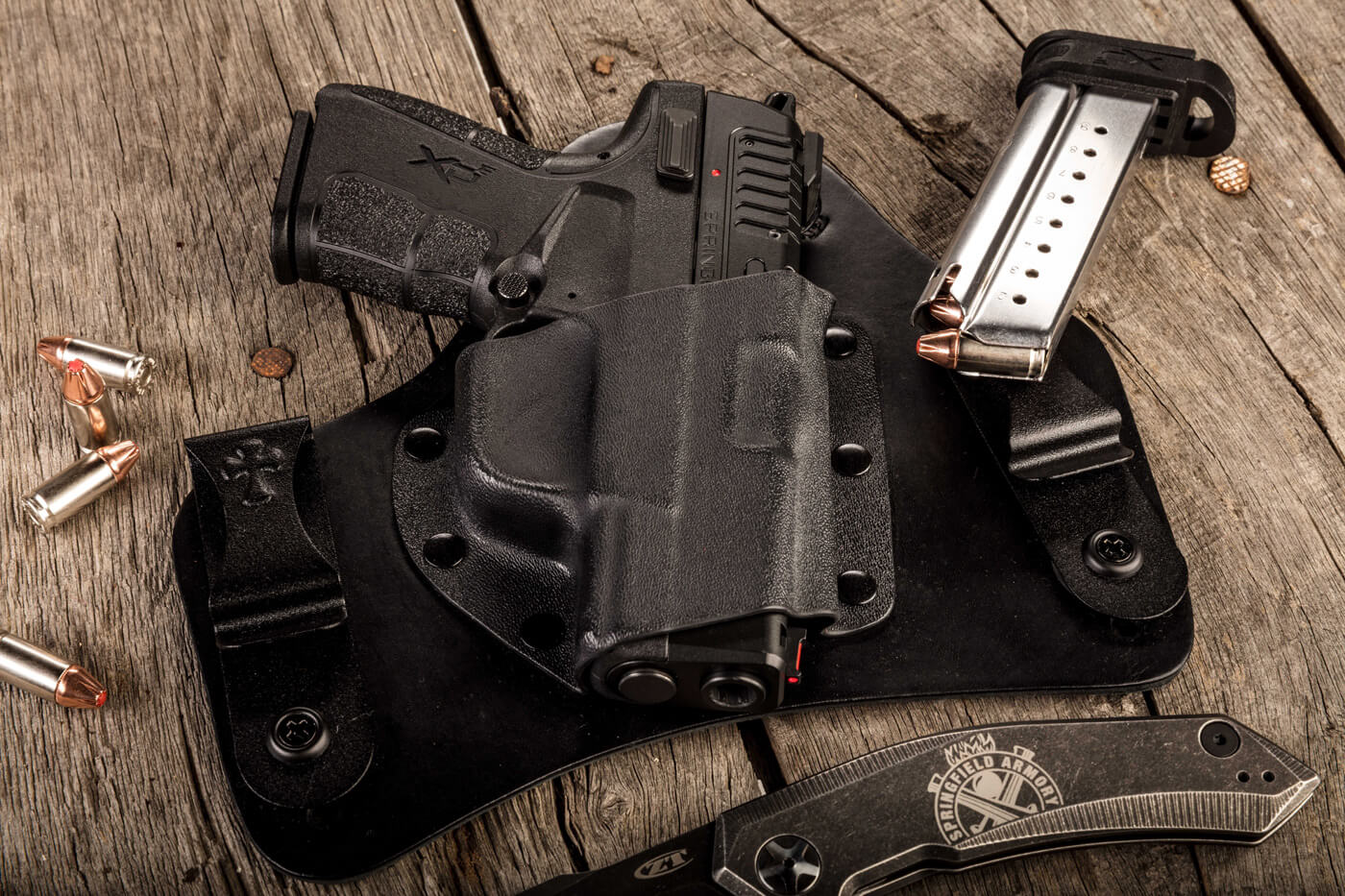 9mm or .45 ACP for concealed carry In this image, we see the difference between .45 and 9mm. Shown is a Springfield Armory pistol, ammunition magazine and a CrossBreed Holster. They are sitting on a table.