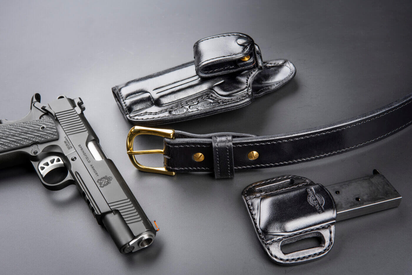 A black Mitch Rosen holster and magazine holder crafted from premium leather are displayed alongside a Springfield Armory 1911 pistol chambered in .45 ACP. These Mitch Rosen holsters demonstrate the luxury firearm holsters' quality and attention to detail. The sleek design supports everyday carry, blending comfort and durability for discerning gun owners. The image emphasizes Mitch Rosen's dedication to handcrafted gun holsters for concealment and secure firearm retention.