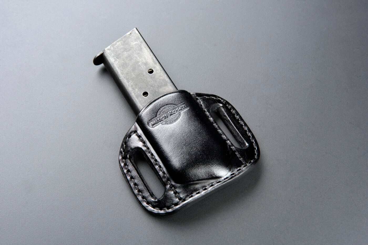 A black leather Mitch Rosen magazine holder with sturdy belt loops is displayed holding a Colt 1911 magazine. The high-quality leather and precise stitching emphasize Mitch Rosen holsters' reputation for durable leather holster materials. This magazine holder is designed for secure and comfortable everyday carry, showcasing Mitch Rosen’s expertise in creating concealed firearm accessories. The sleek design combines functionality with leather craftsmanship for holsters and accessories.