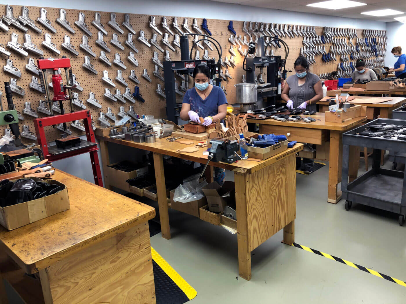 Workers at the Mitch Rosen factory are shown carefully assembling leather holsters, with tools and machines visible in the background. This process illustrates the artistry and skill behind Mitch Rosen holsters, emphasizing their reputation for premium firearm holsters. The factory environment underscores the blend of modern techniques and traditional leather craftsmanship. This photo highlights the expertise that goes into producing comfortable holsters for everyday carry and personal defense.