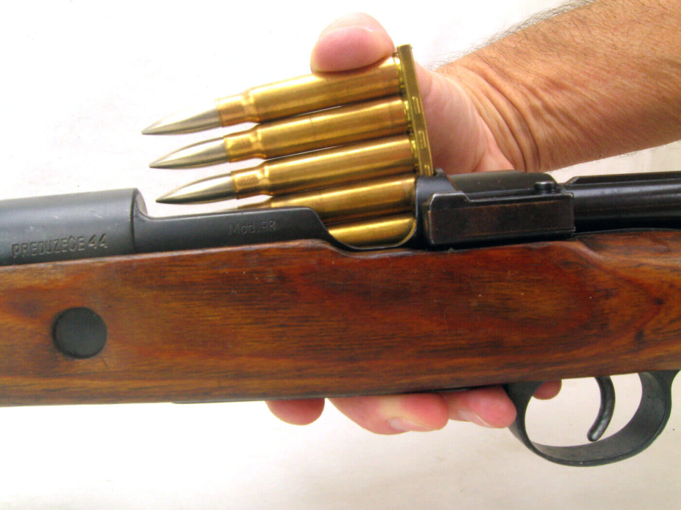 A man carefully loads a vintage military rifle using a stripper clip during a Vintage Military Rifle Games competition. The action emphasizes the skill and techniques required to operate historical firearms authentically. His focused expression and the rifle's detailed components highlight the dedication to preserving military history. This moment showcases the hands-on engagement and marksmanship celebrated in the Vintage Military Rifle Games.