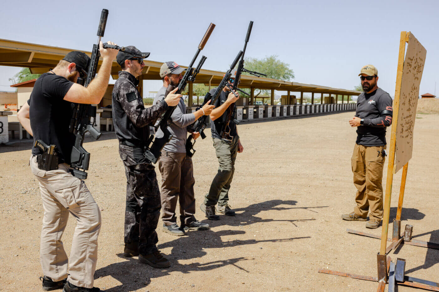 Men standing with rifles while being instructed at precision rifle school