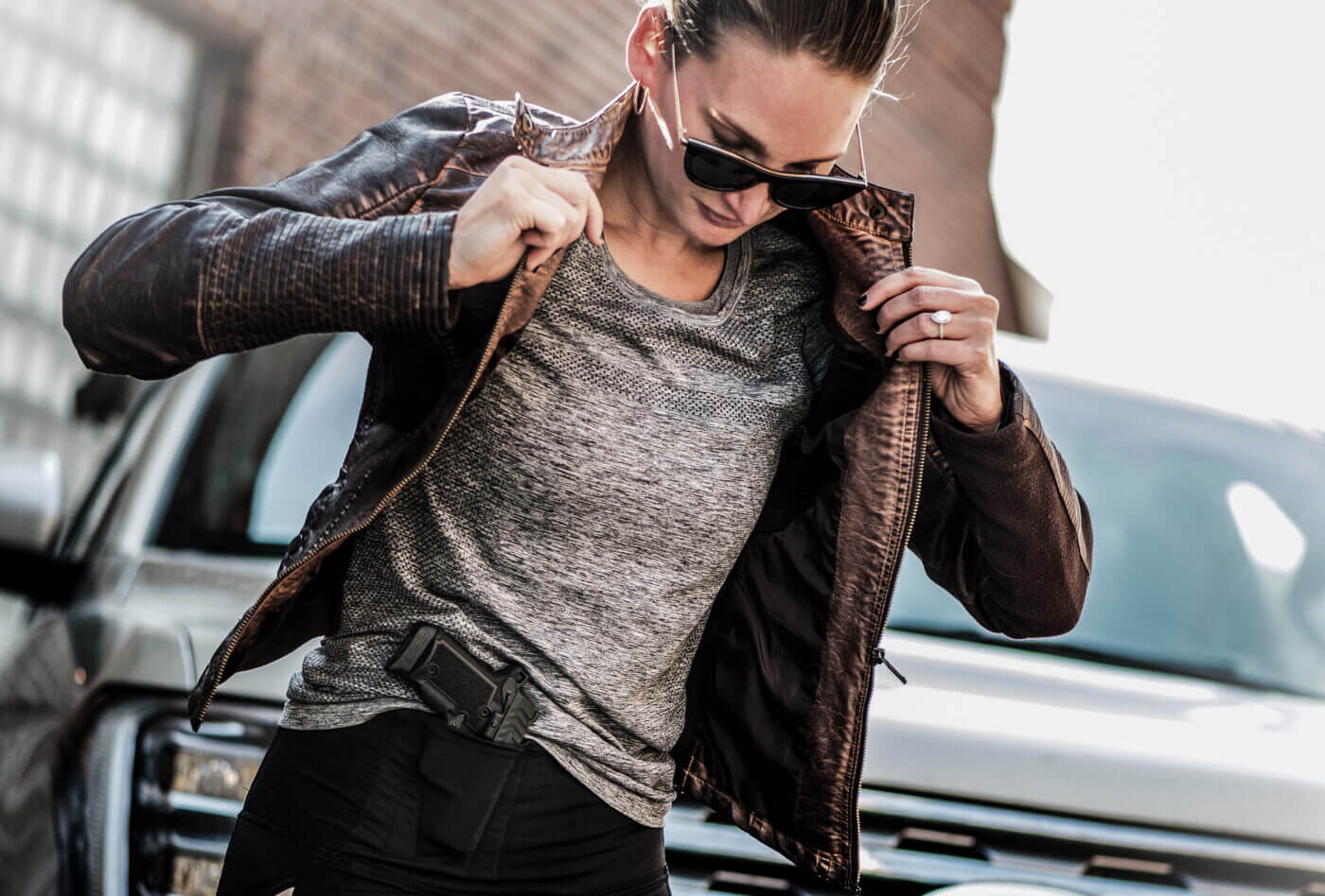 Woman putting on jacket with gun in waistband holster