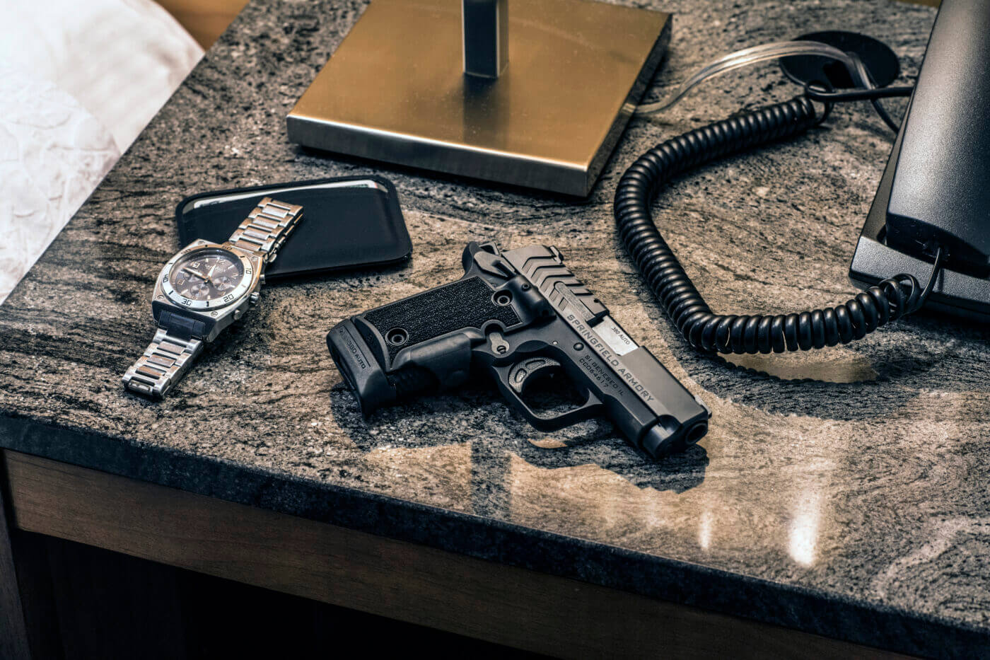 A Springfield 911, a wallet, and a watch on a nightstand