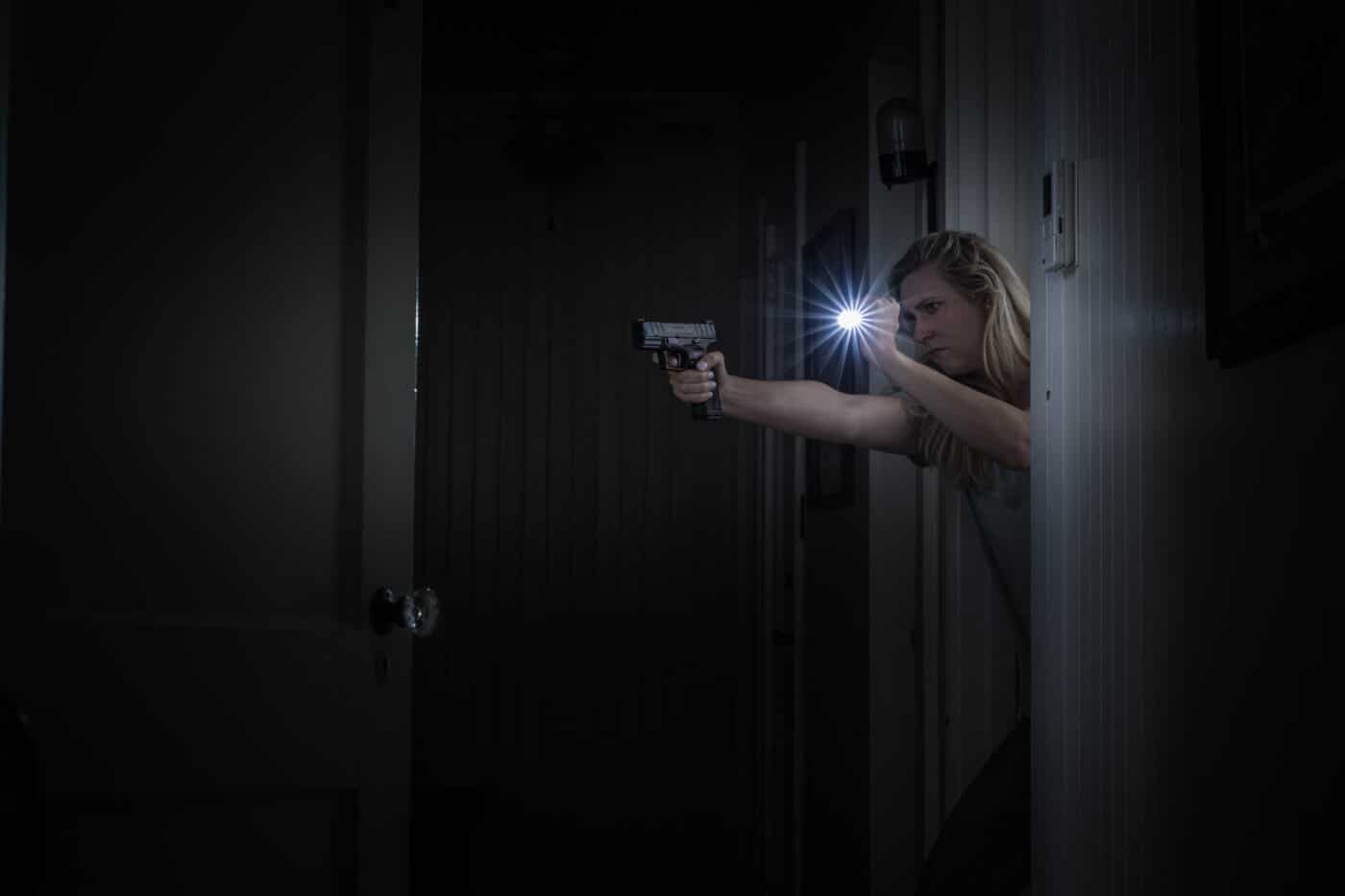 Woman shooting pistol at night in her home while holding a light