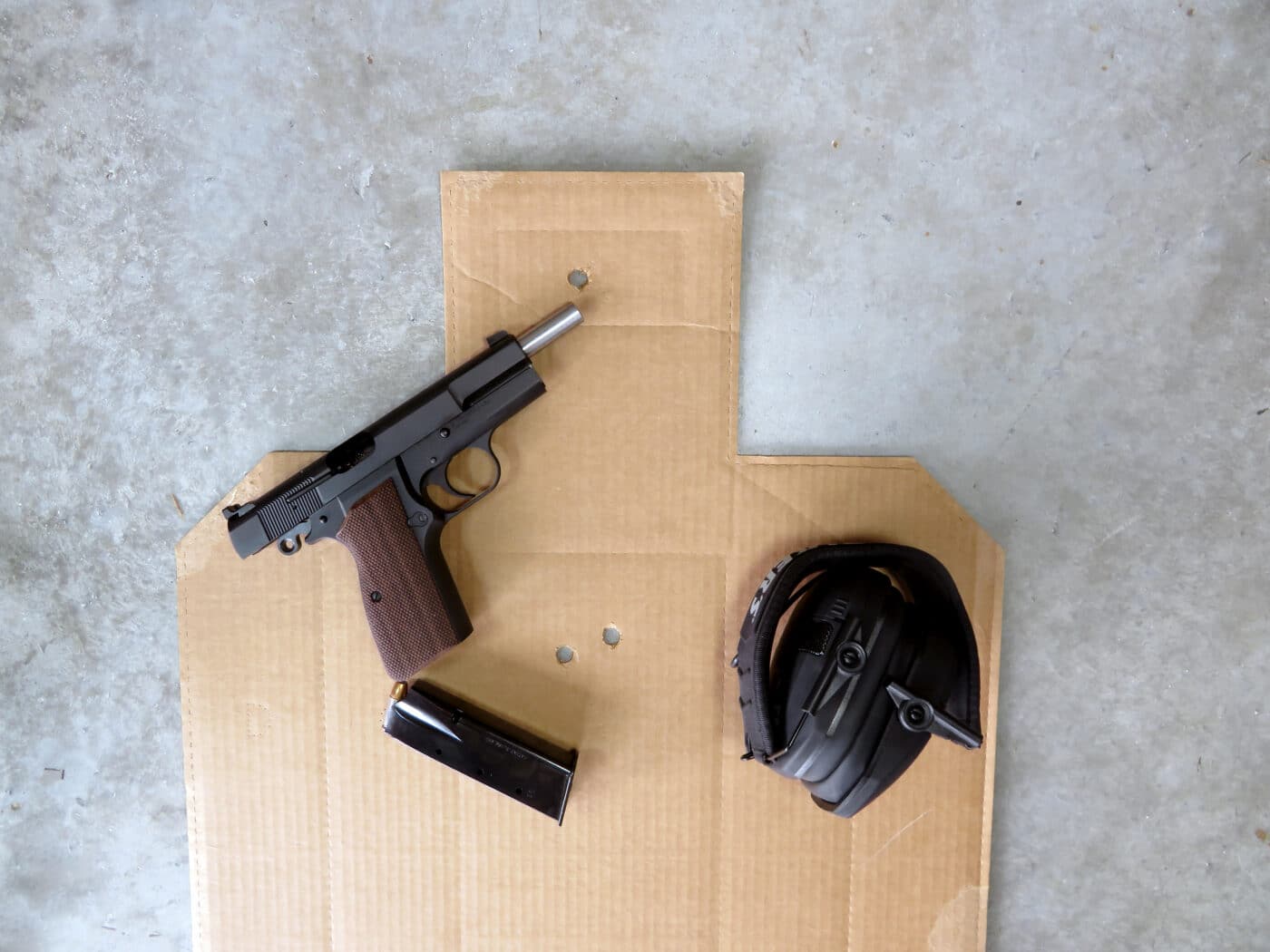 Pistol with magazine and ear protection on top of cardboard shooting target
