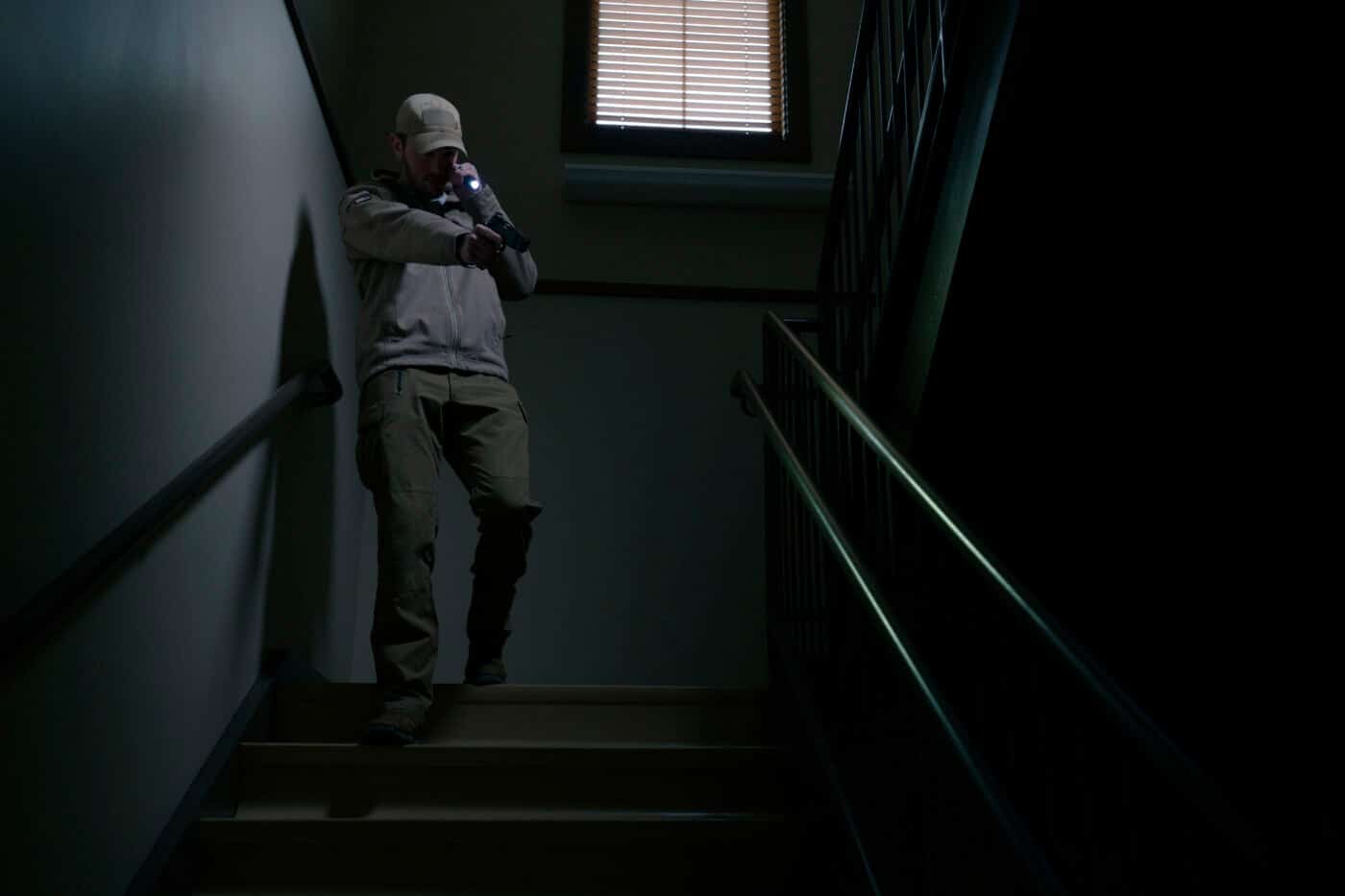 Man carrying a pistol and handheld light in a dark stairwell