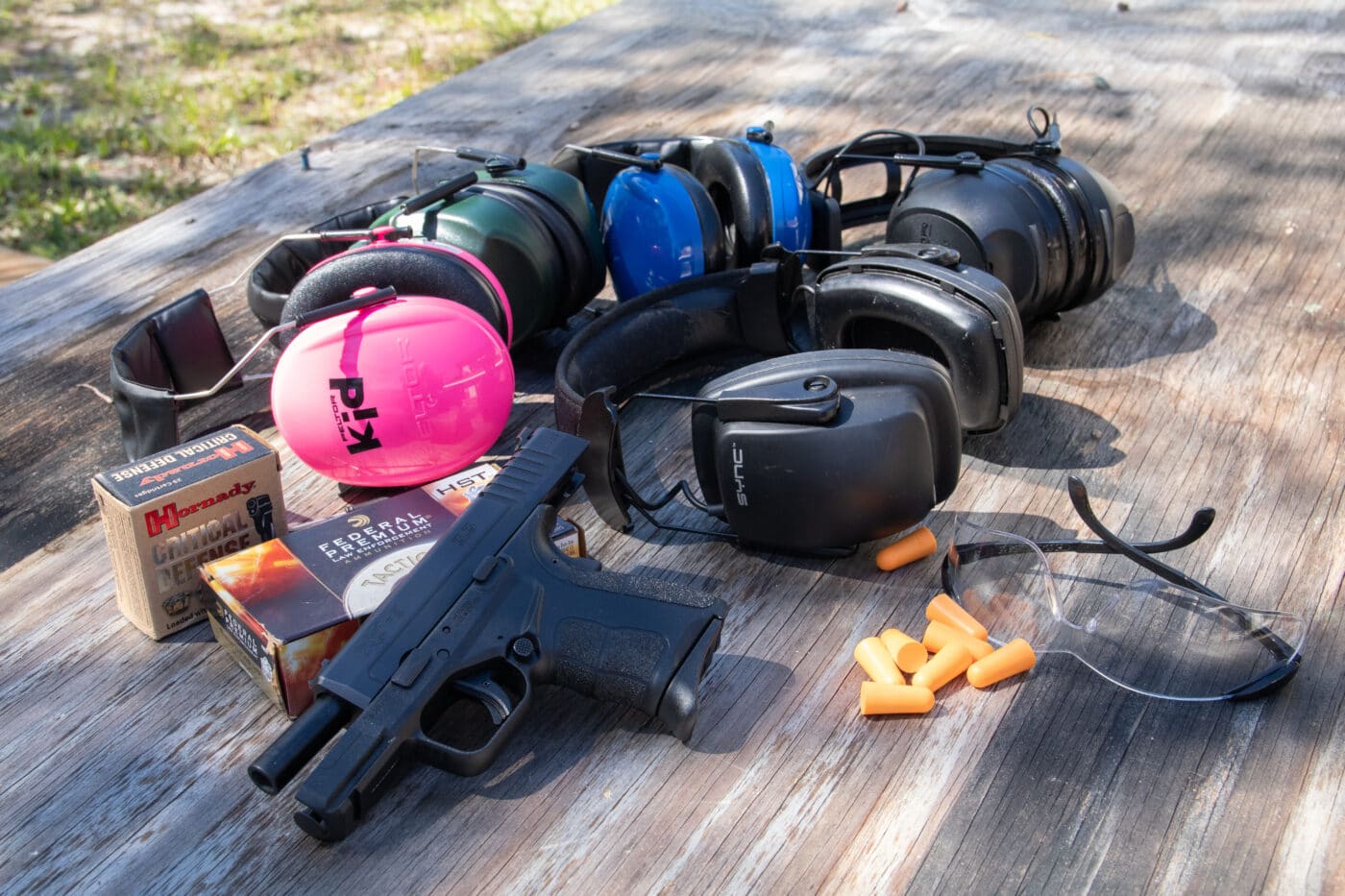 Variety of different types of ear protection on table next to pistol and ammo