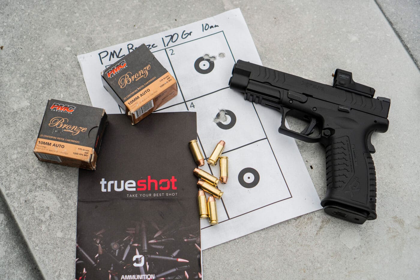 Springfield XD-M Elite 4.5" 10mm pistol and ammo resting on top of target used for accuracy testing as well as a True Shot brochure