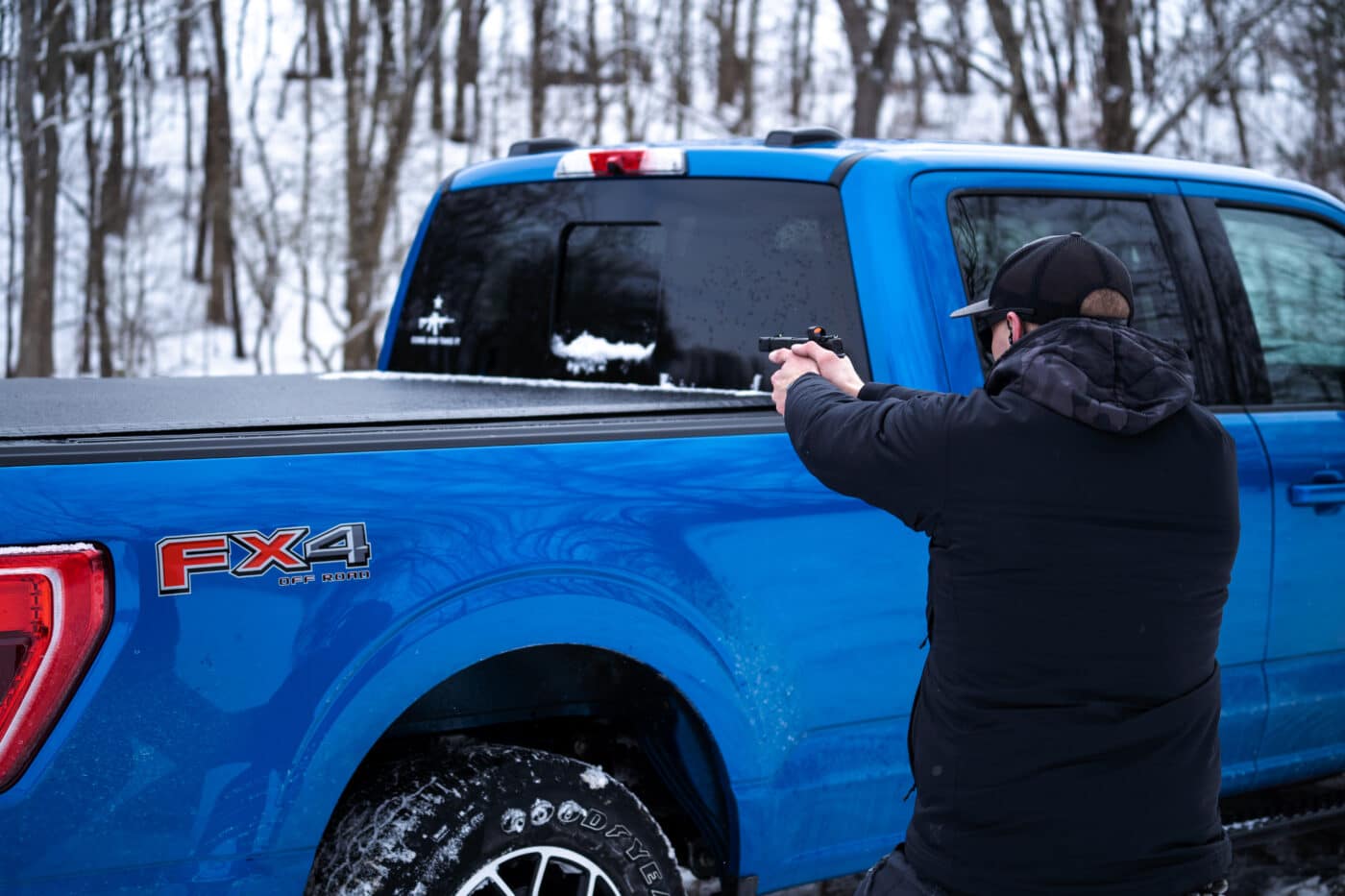 Man using a pickup truck for cover in a mock gunfight. This is self-defense firearms training using a vehicle.