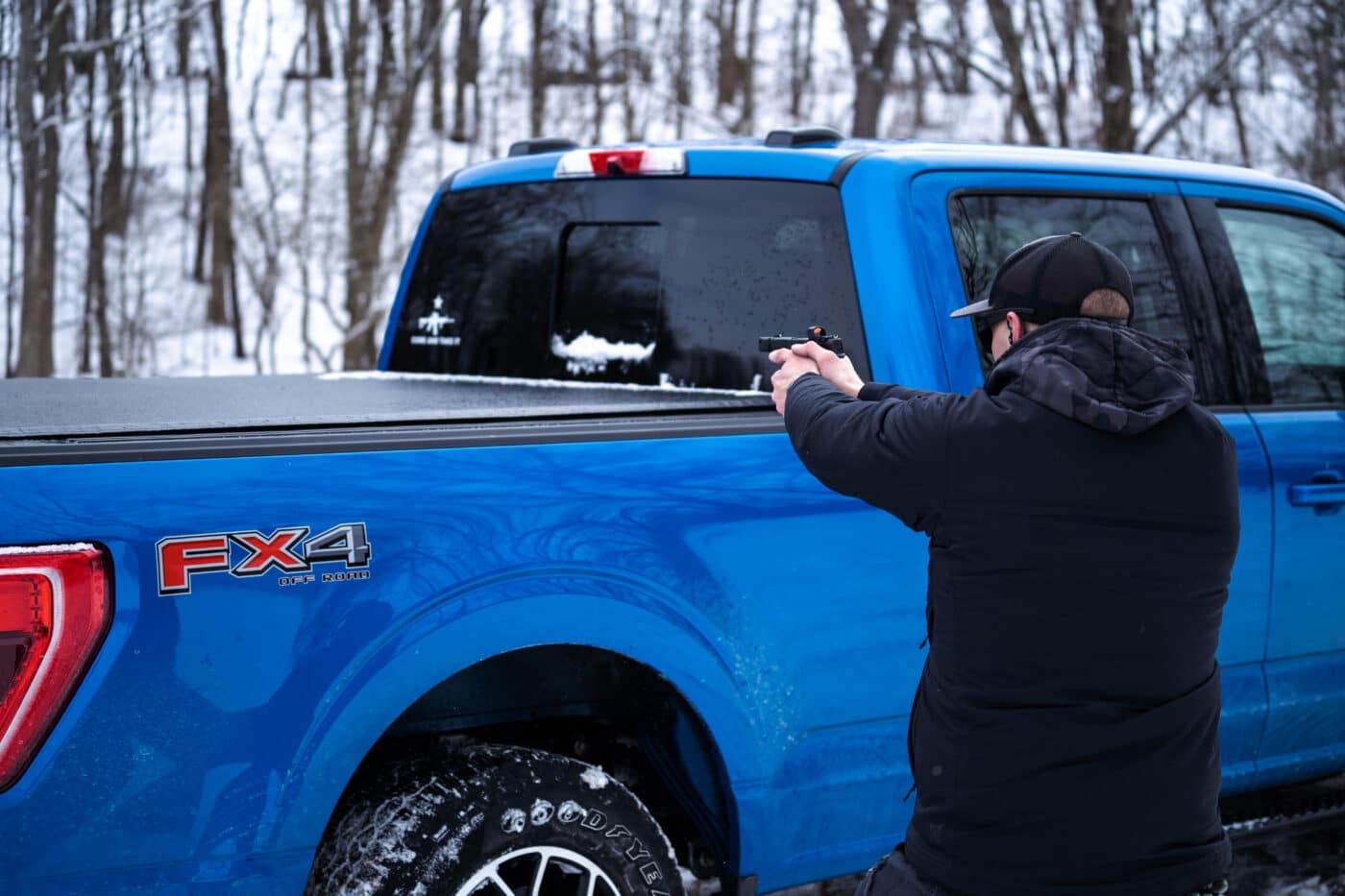 Man using a pickup truck for cover in a mock gunfight