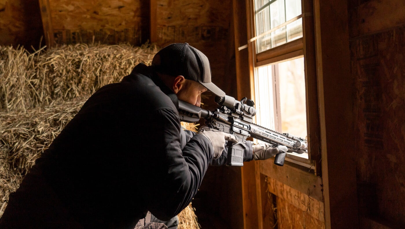 Man testing trigger on SAINT Edge for rural defense rifle while shooting out a barn window