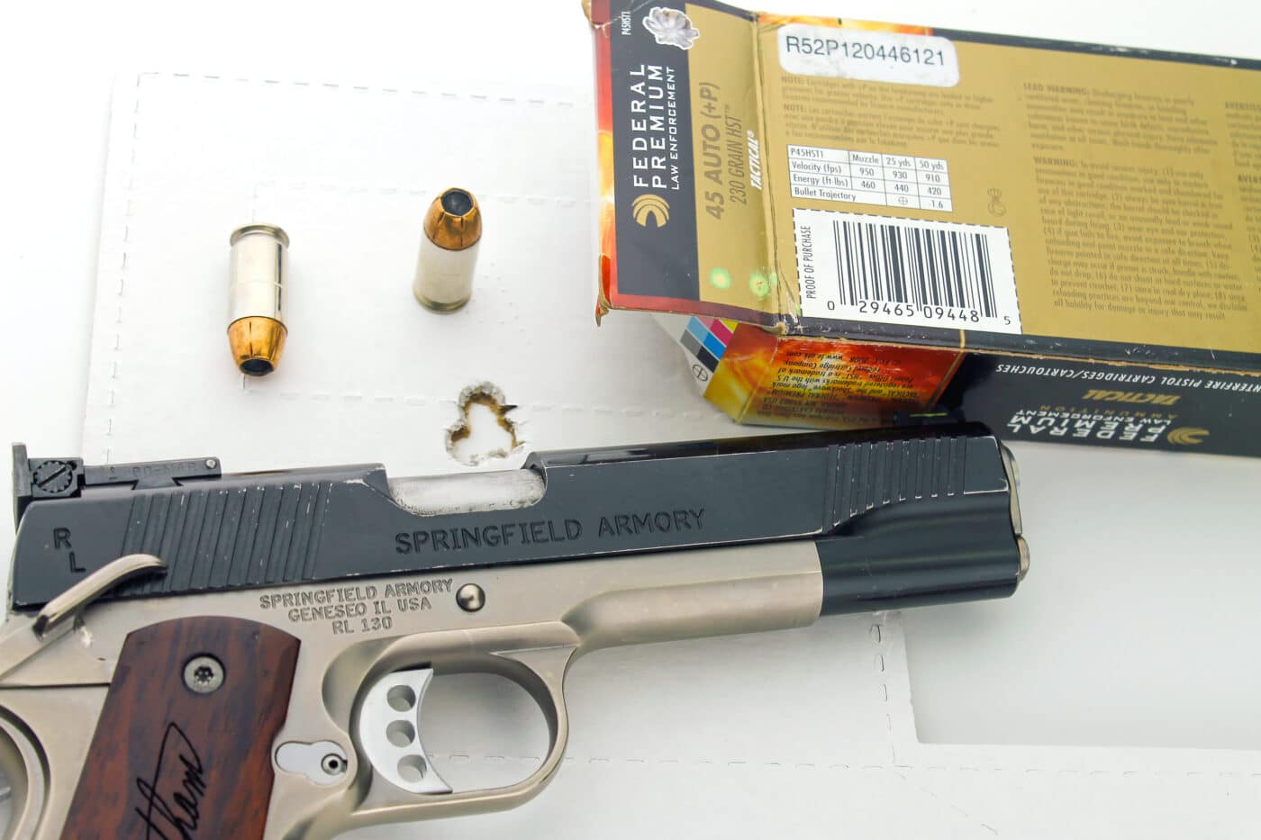Springfield 1911 in .45 ACP next to a box of ammo, both on top of a target shot by Massad Ayoob with the pistol