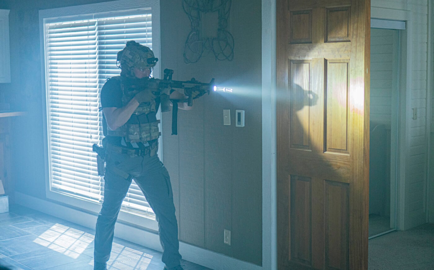 Person in tactical gear with flashlight mounted on home defense AR-15 rifle