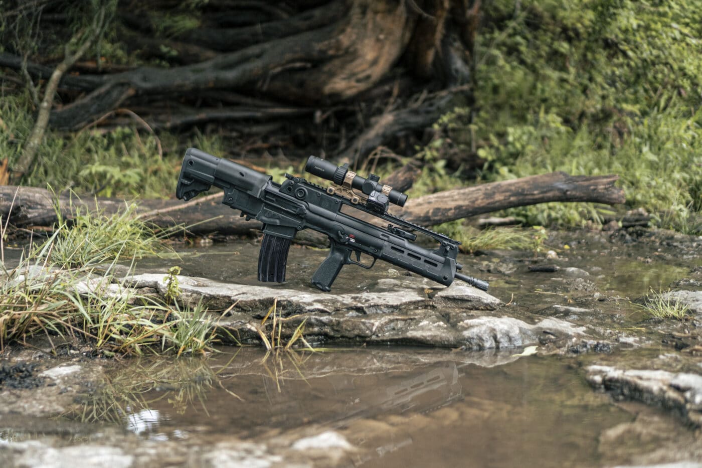 Leupold scope on a Springfield Hellion bullpup rifle leaning up against a log in a streambed