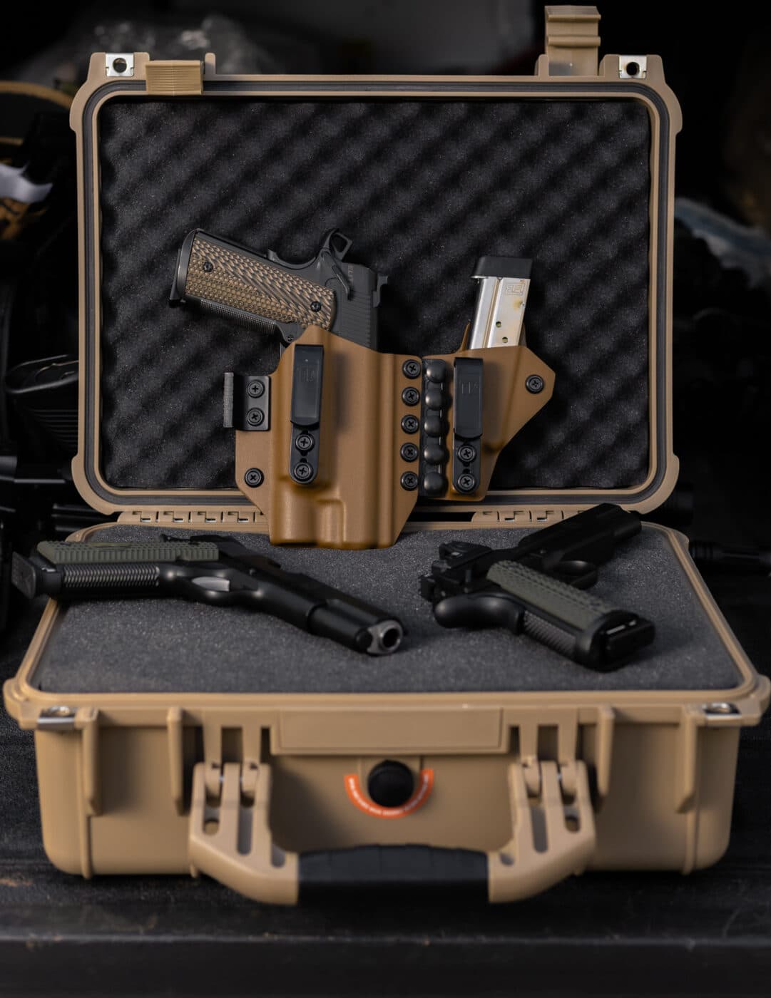 A 1911 pistol inside a holster next to two other pistols in a case