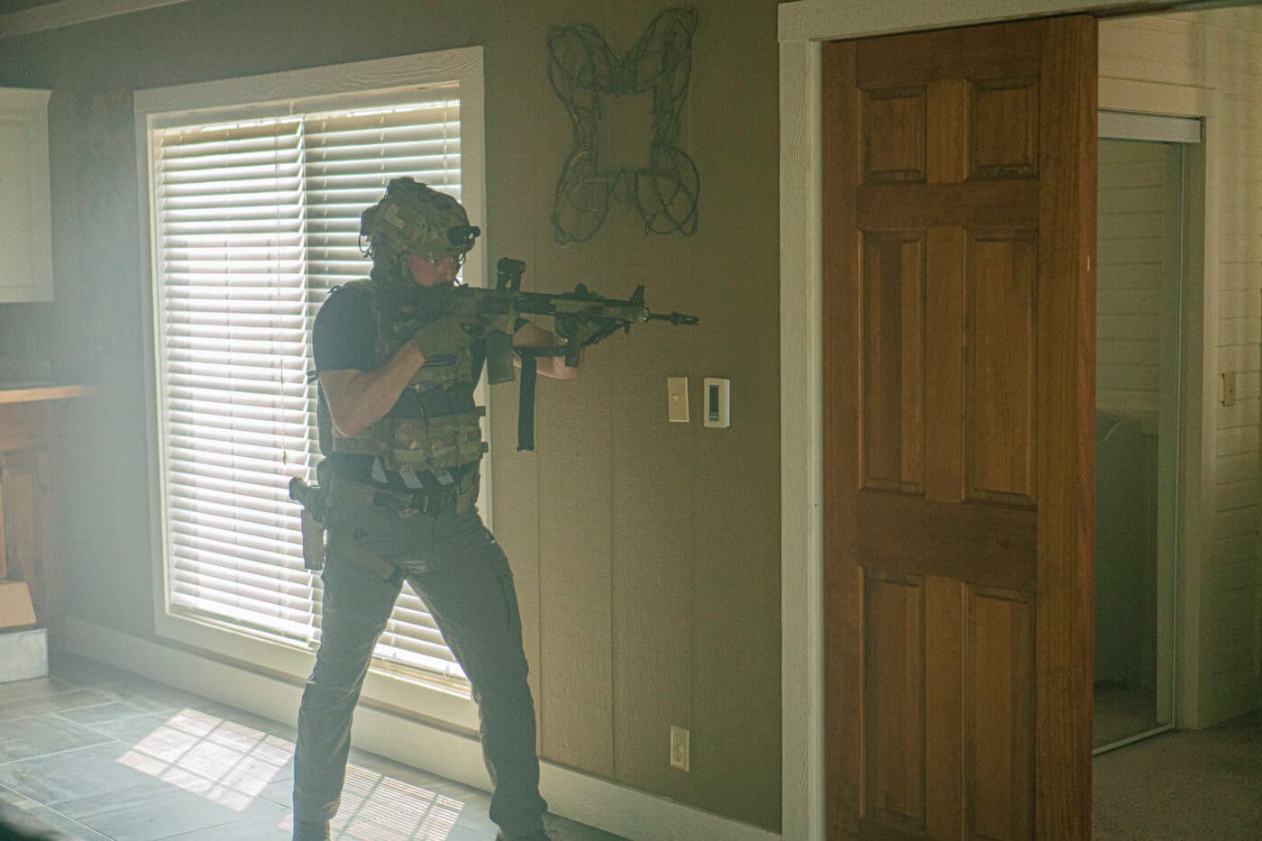 Man with a rifle looking through a doorway while clearing a house