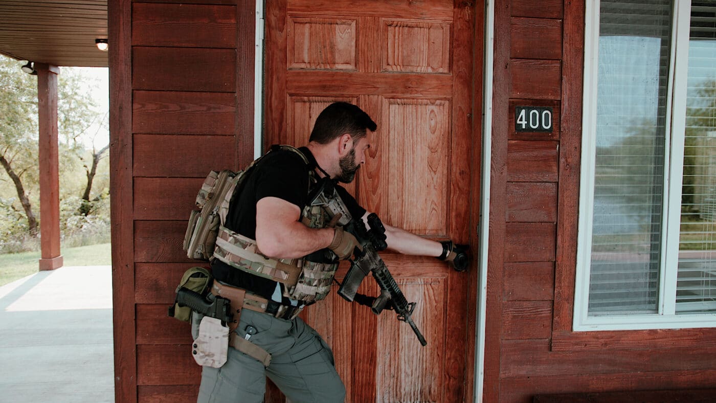 Man carrying a rifle and entering a house to start clearing it
