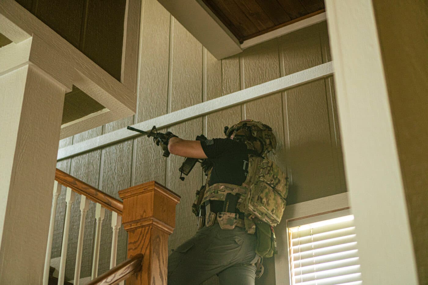 Man ascending stairs while carrying a rifle to clear a home