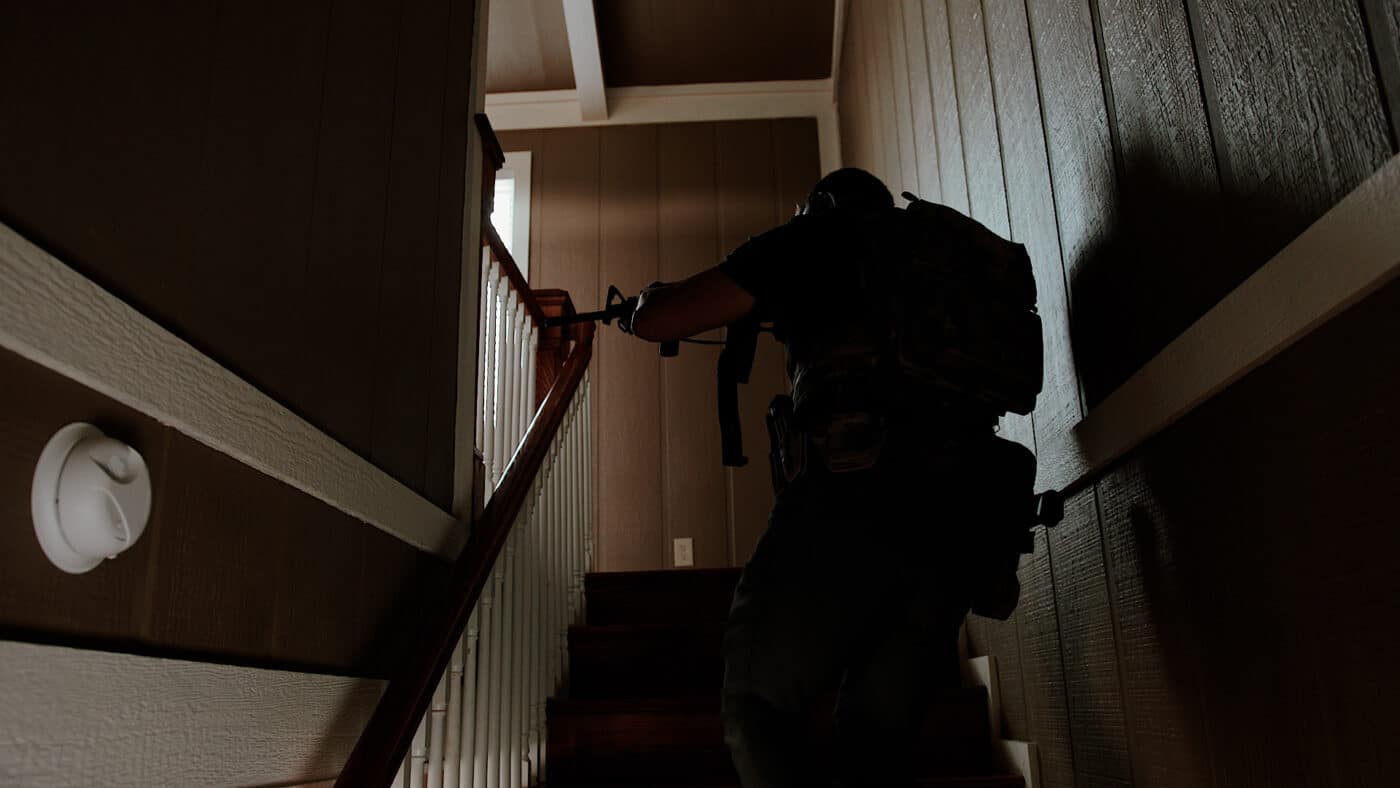 Man ascending stairs while carrying a rifle to clear a home