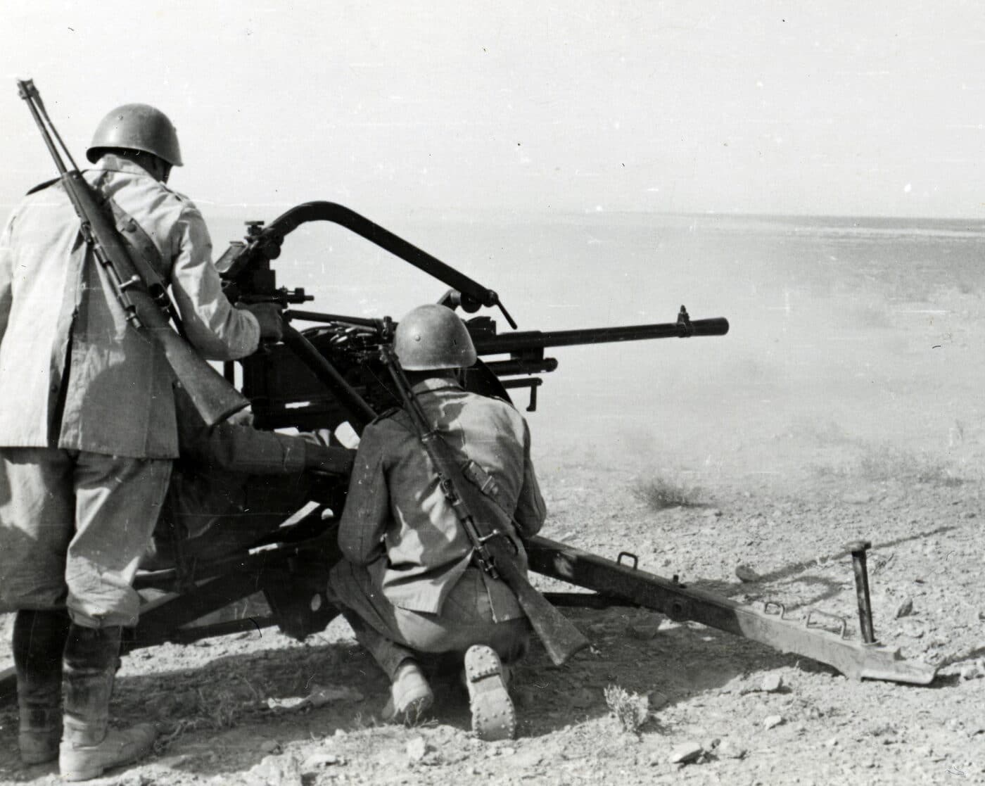 Italian Carcano carbines on soldiers backs while they are firing a Breda 20mm in North Africa