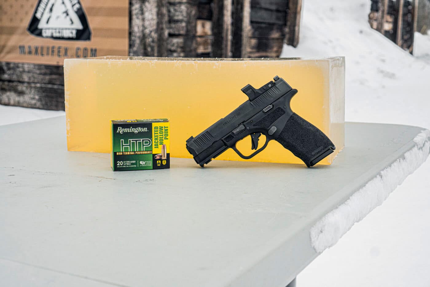 Box of Remington HTP ammo and Springfield Hellcat Pro pistol sitting next to a block of ballistic gel