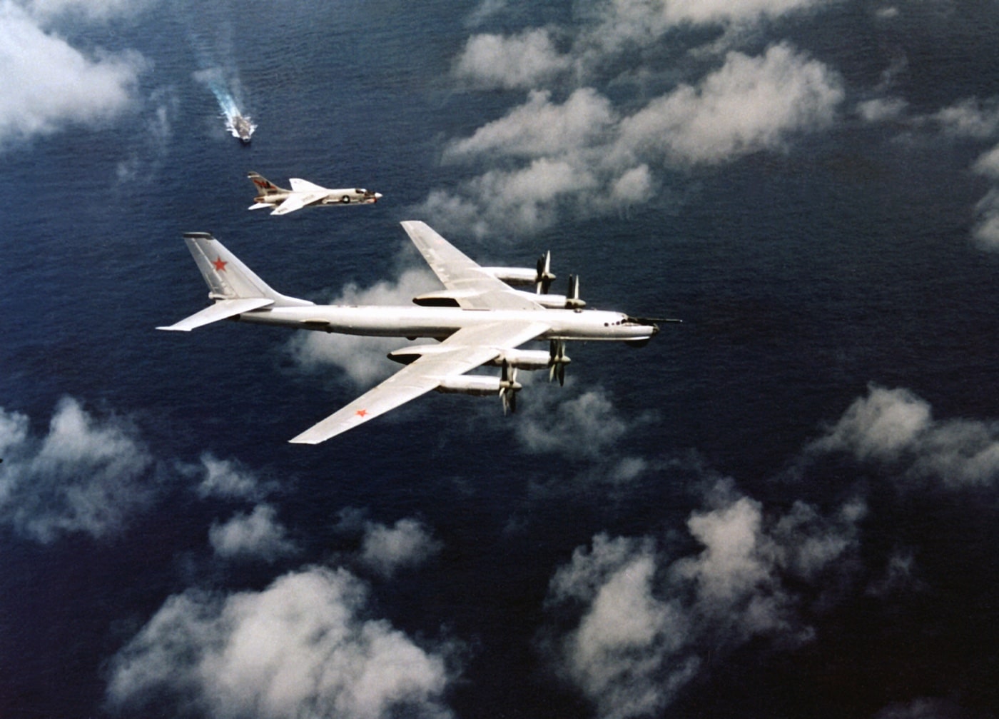 In this photo, an F8U Crusader escorts a Soviet Union TU-95 Bear bomber away from a U.S. Navy carrier group during the Cold War. The Crusader design was a carrier based fighter that was more than a match for the Russian MiG-17s and somilar communist aircraft of the era. It was equipped with guns and missiles for air-to-air combat. In an era of jets, the Chance Vought fighter was designed with guns. 