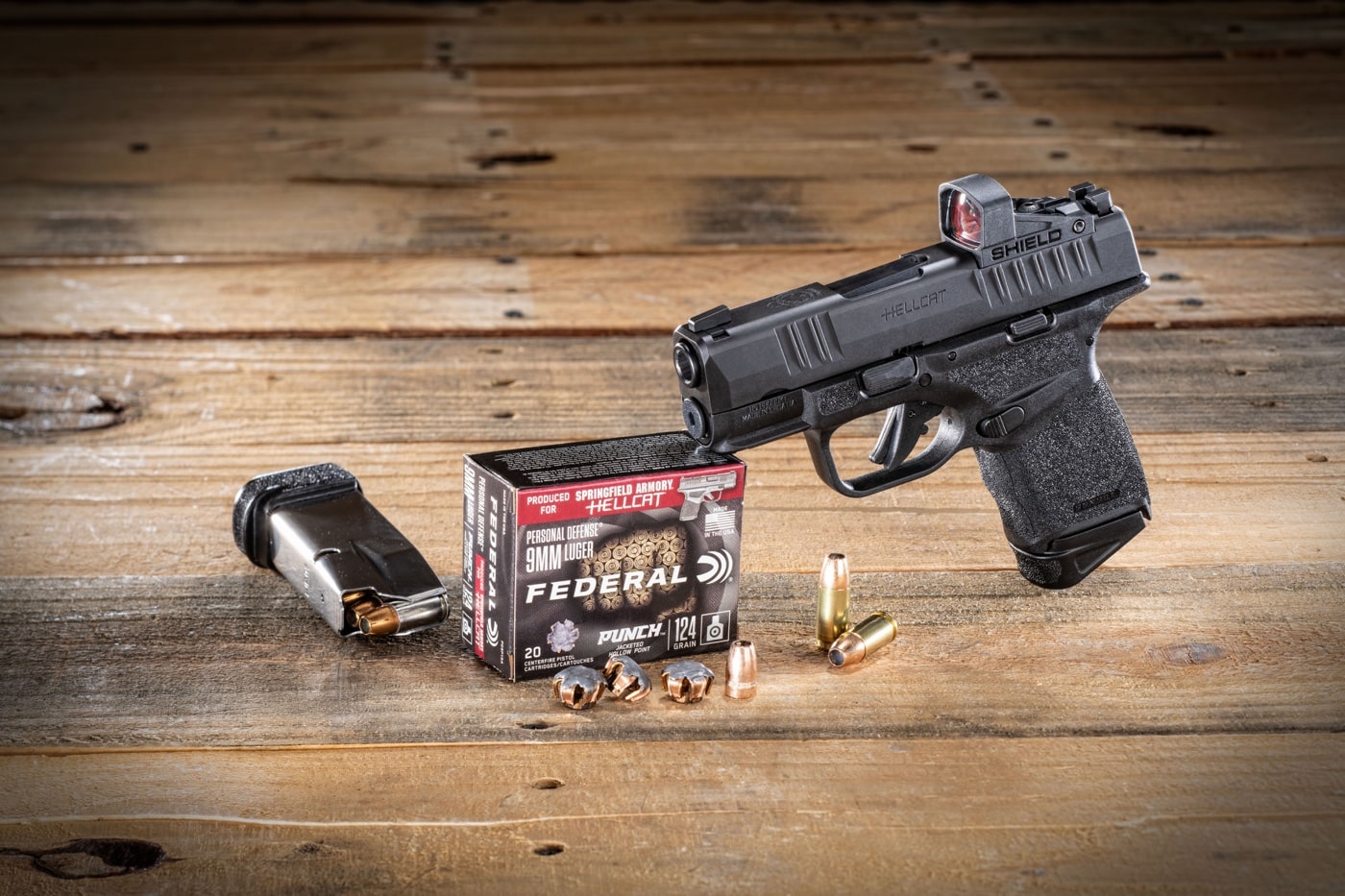 In this image, the the author placed the Federal Punch 9mm ammo next to the Springfield Armory Hellcat pistol. Also seen in the image is a spare magazine, bullets, expensed bullets and loaded cartridges. A Shield red dot sight is the optic mounted on the slide of the CCW handgun.