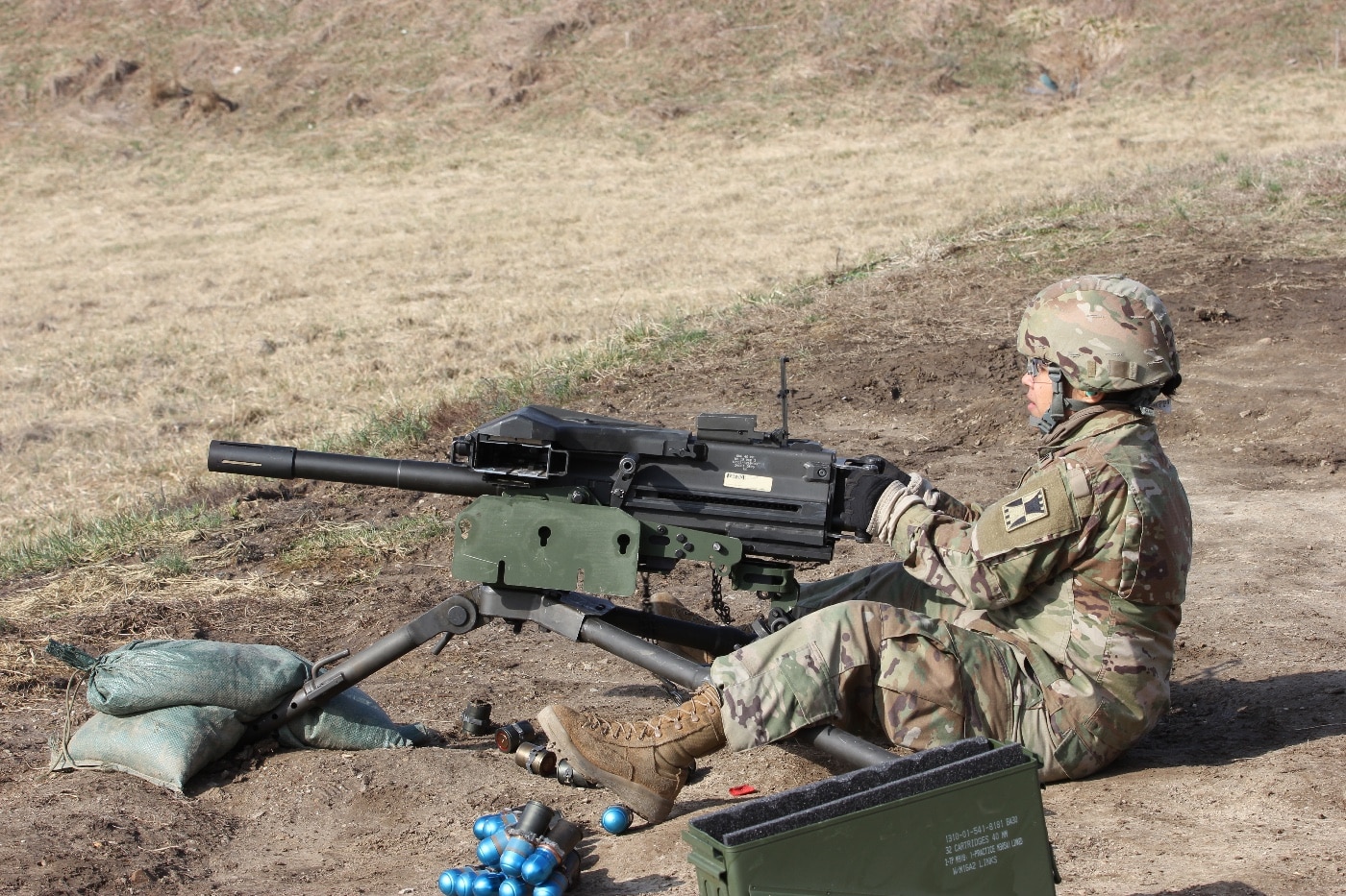 The image shows a U.S. Army soldier firing the Mk19 automatic grenade launcher during a training exercise in Indiana. The Mk19 is a belt-fed, crew-served automatic weapon that launches 40mm grenades at the enemy. Also known as 40 mike mike, these rounds come in a variety of packages including high-explosive and anti-armor. These weapon systems are dual-purpose, allowing for both direct and indirect firing of 40 mm rounds. They are used by the Army and Marine Corps.