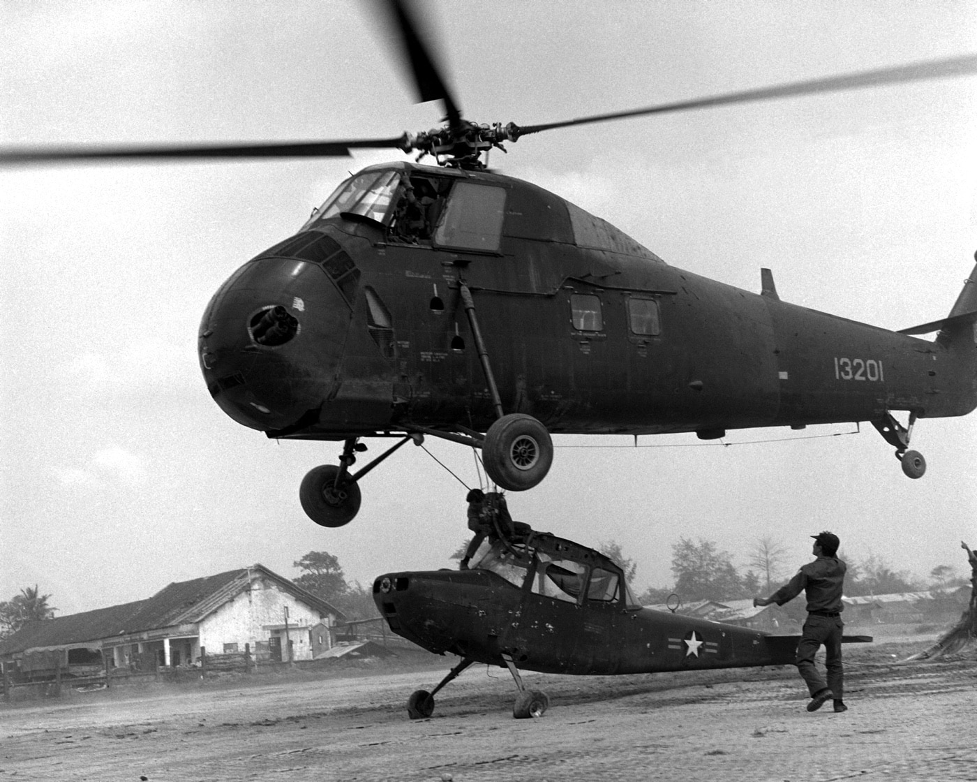 In this photo a Republic of Vietnam Air Force H-34 Choctaw lifts a damaged O-1 Birddog from the tarmac at Da Nang Air Base. The O-1 was a fixed wing observation airplane used for artillery spotting and guiding airstrikes against the enemy NVA and VC forces. Like the Choctaw, it was a tail dragger and piston powered.