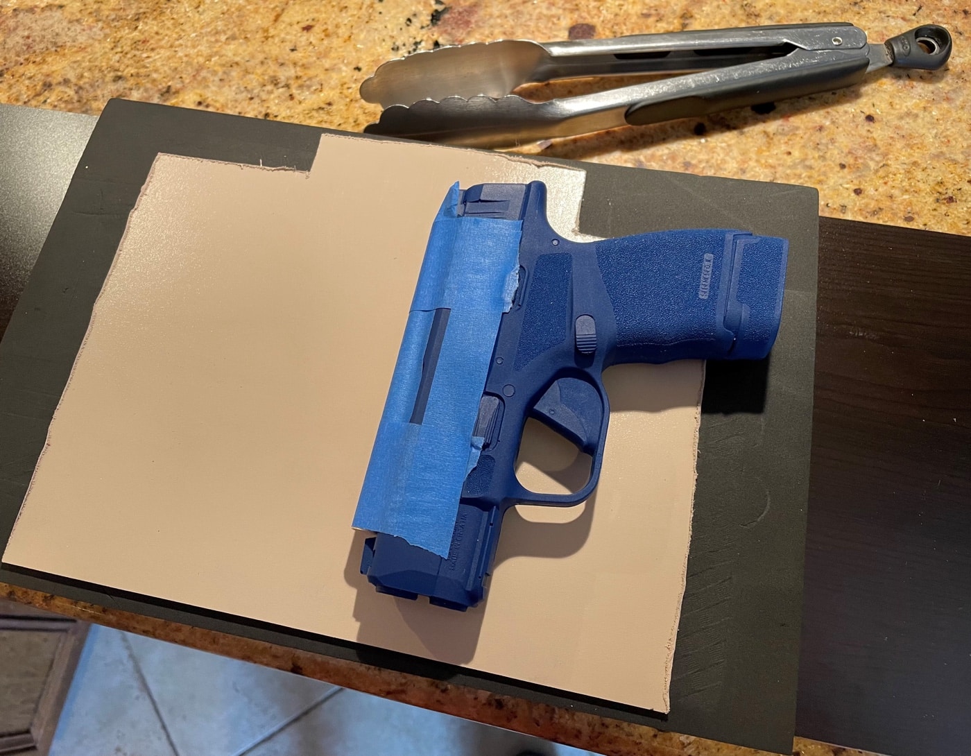 In this photo, the author is using his Blue Gun mold to test fit the pistol on the Kydex sheets as he want to make sure the size — height and width — appears correct. It doesn't need to be perfect — if there is some overlap of extra material — that's fine. Use a pencil to trace in where you want things to be, but you can use a sander later to remove the excess material.