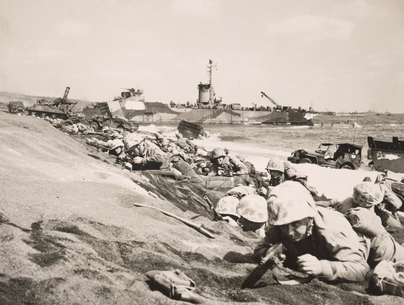 In this digital reproduction of a photograph, we see Marines who landed on the island crawling through the sands of Iwo Jima. An epic battle, Iwo Jima provided a stepping stone to the ultimate invasion of mainland Japan. The Iwo Jima Marine Corps War Memorial in Arlington, Virginia is based on the second flag raised at the summit of Mount Suribachi. It was a larger flag in the popular Marines raising the American flag photos and video.