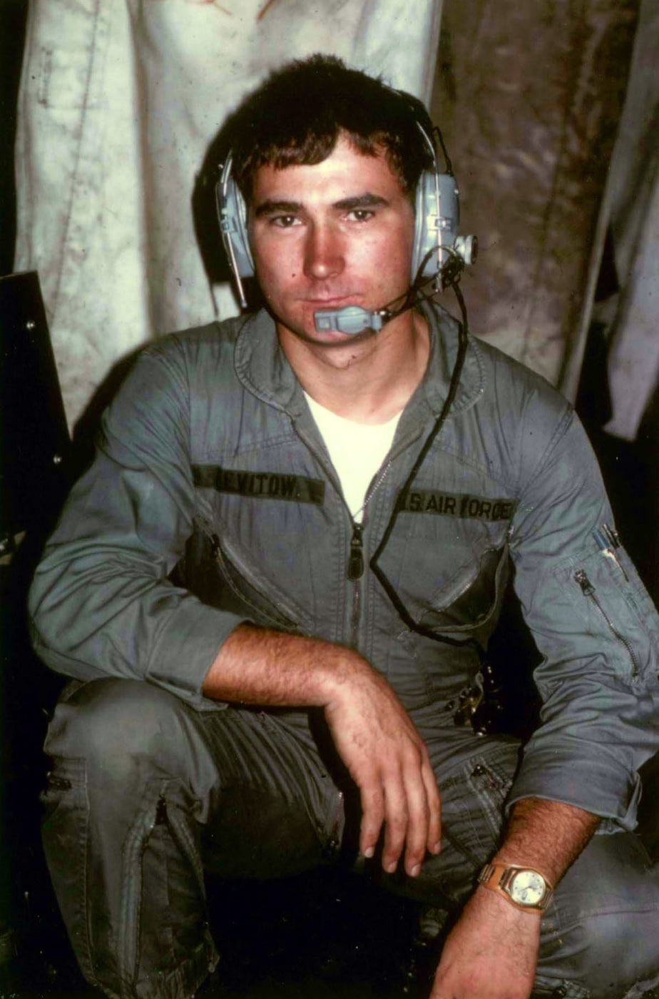 In this photograph, we see Airman 1st Class John Levitow. Levitow is wearing his uniform, an Air Force flight suit, and a radio headset so he can communicate with the pilot and other members of his military unit. Levitow received the Medal of Honor for gallantry in combat during a military operation on February 24, 1969.