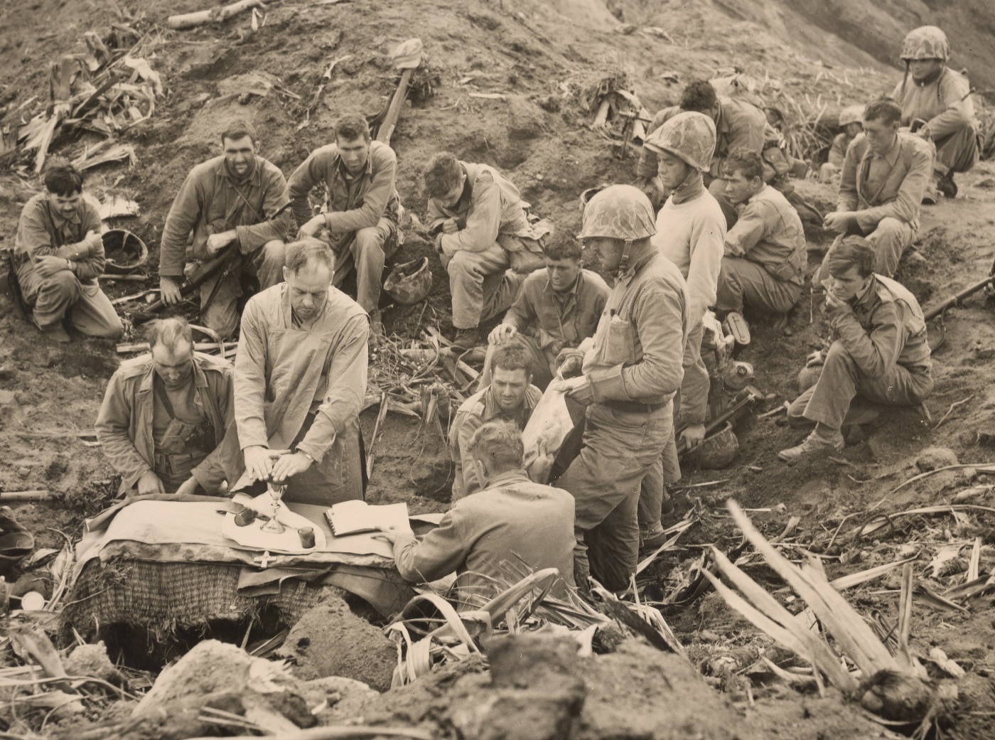 Catholic Mass is celebrated on Iwo Jima. Two Marines wearing helmets shield the improvised altar from high winds that rake the volcano summit. Image: Sgt. Lou R. Burmeister/U.S. Marine Corps