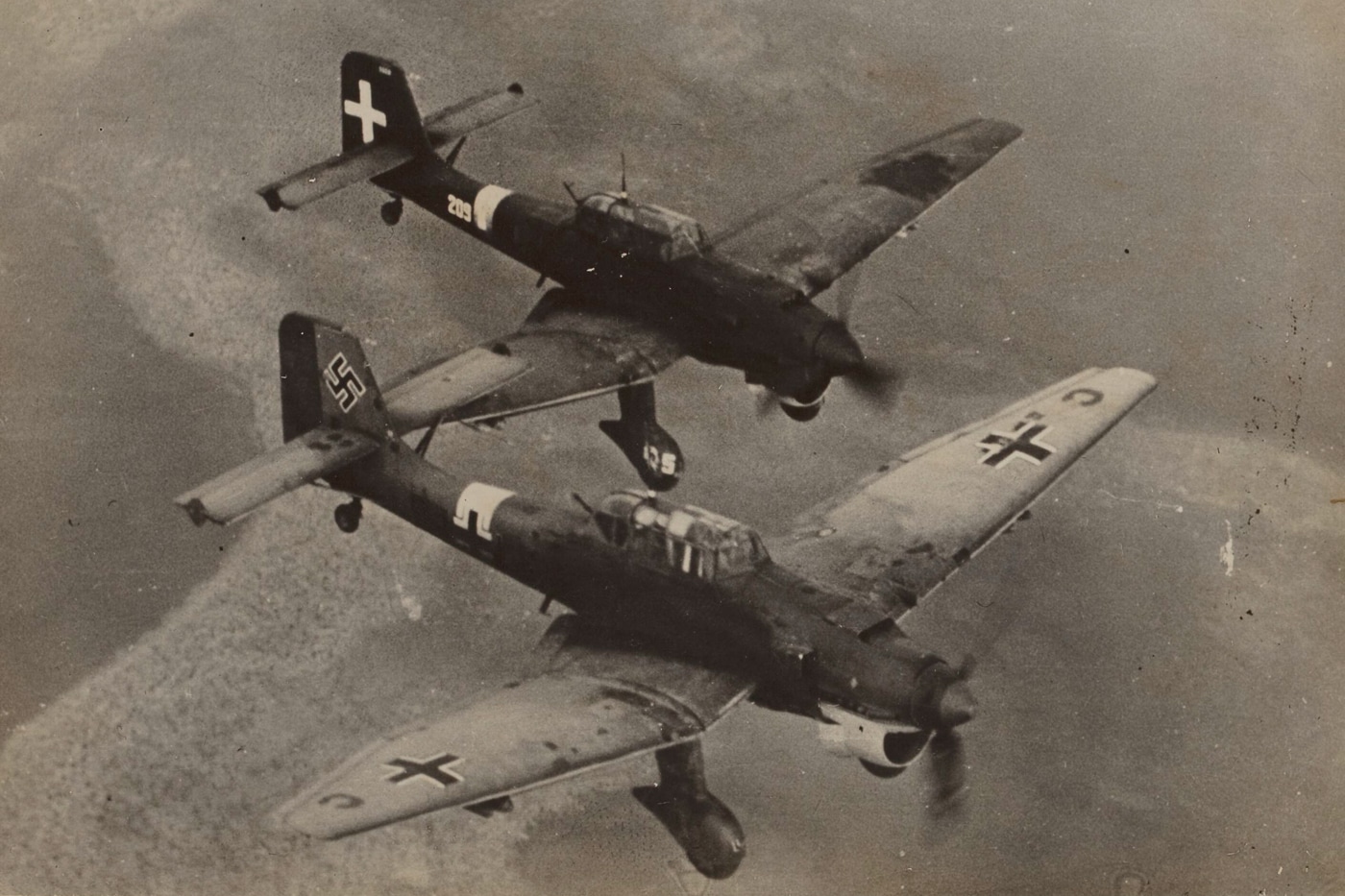 In this photo we see an Fascist Italy Air Force Stuka flying in formation with a Nazi Germany Stuka. The Italian Air Force is the air force of the Italian Republic. The Italian Air Force was founded as an independent service arm on 28 March 1923 by King Victor Emmanuel III as the Regia Aeronautica. The Kingdom of Italy was governed by the National Fascist Party from 1922 to 1943 with Benito Mussolini as prime minister and dictator.