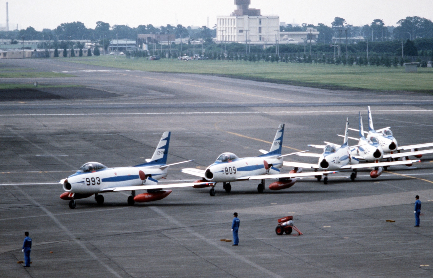 In this photo we see five F-86 jets taxi on a runway in Japan. These jets are part of Blue Impulse — the flight demo team for the Japanese Air Self Defense Force. This demo team is similar to the Blue Angles and Thunderbirds in the United States. Japan was one of several countries that purchased F-86 fighters from the USA.