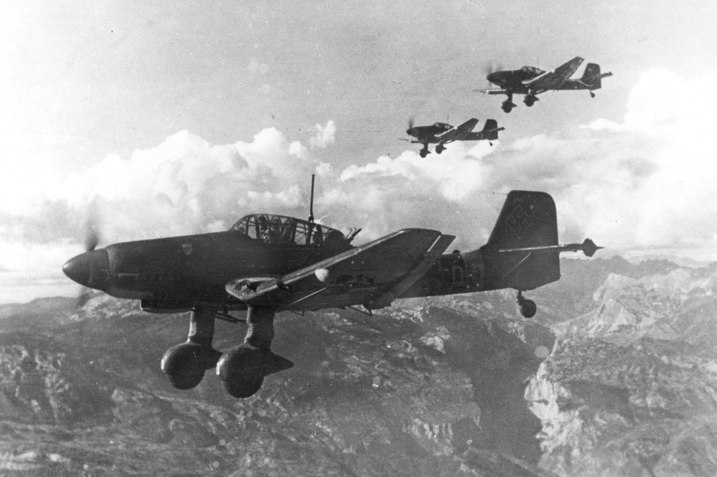In this vintage photograph, we see a three plane formation of a German air force Ju 87D dive bombers enroute to attack Yugoslavian partisans fighting the Nazis. From the cockpit, a pilot could make the Junkers dive and attack infantry positions. In fact, Stukas dropped the first bombs of the war in the European War. Stukas went deep behind enemy lines to strike soft targets and could dive on many otherwise inaccessible targets due to the unique Stuka design. However, the planes were easy targets for enemy fighters and Stuka losses increased throughout the war.