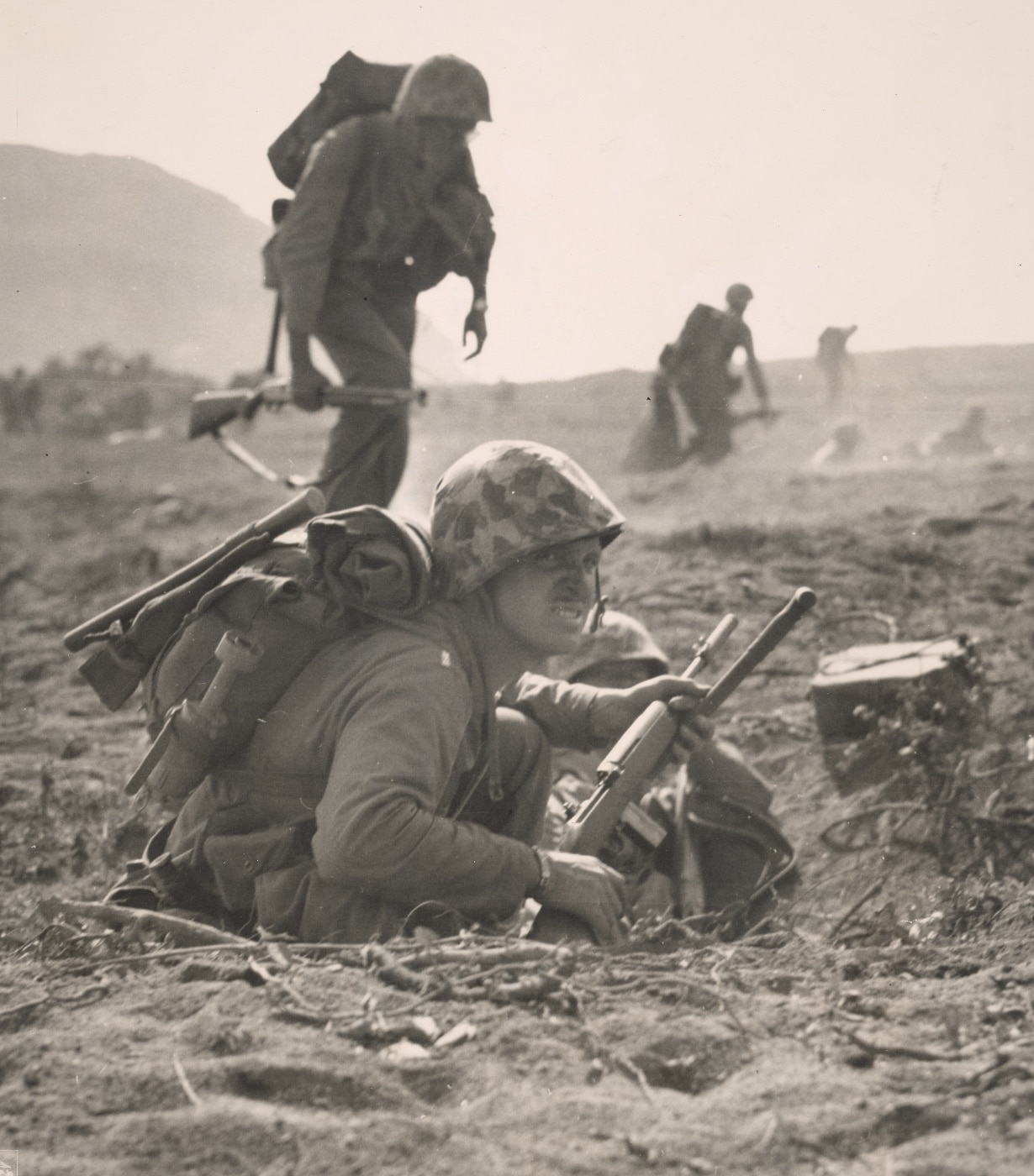In this photo we see a U.S. Marine with a M1 Carbine that has a rifle grenade attachment and ammunition. Behind him is another Marine carrying a 12 gauge shotgun. These were common firearms carried by American troops in this part of the island. 