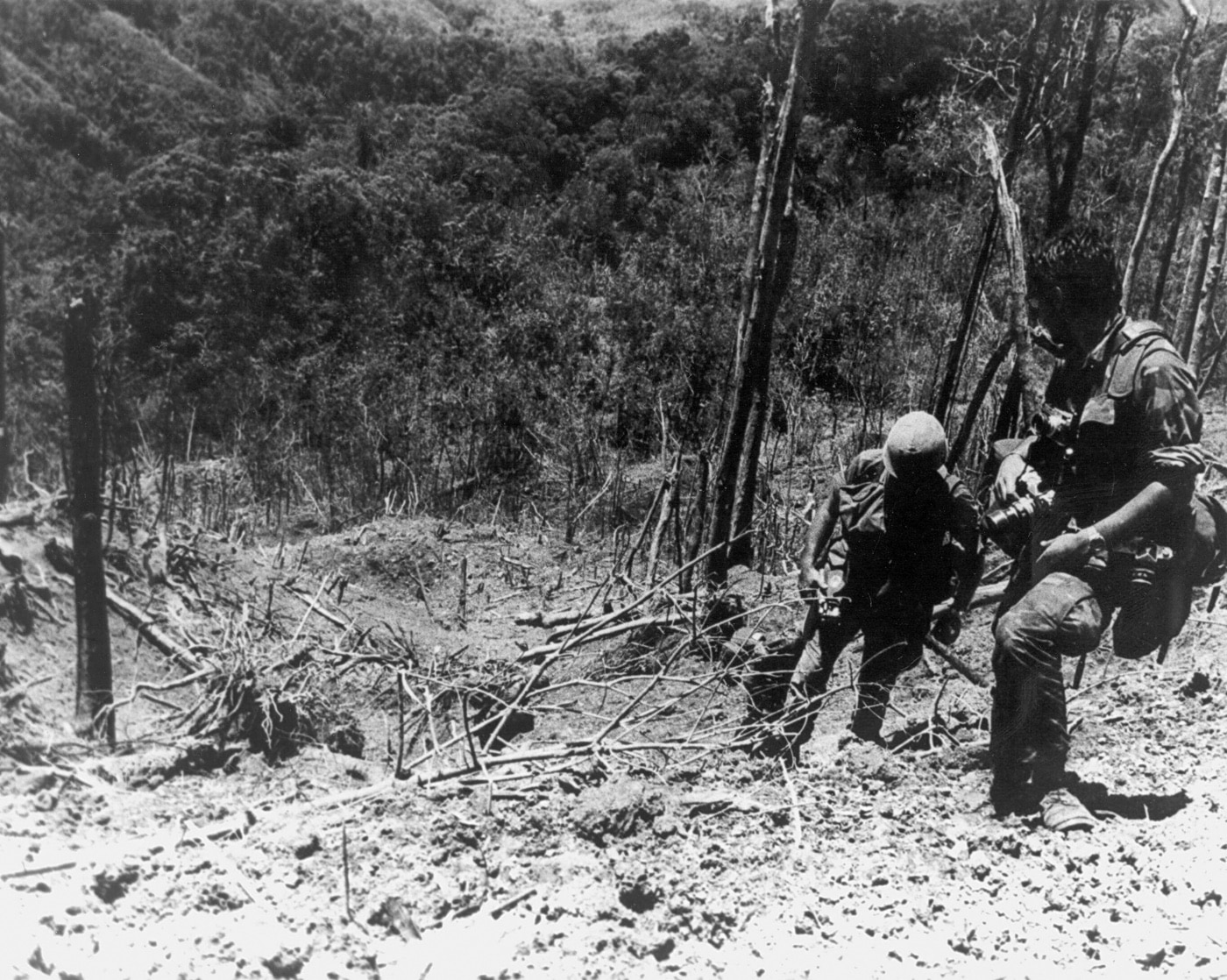 In this image, U.S. soldiers are climbing Hamburger Hill. On the right side of the photo is an Army photographer.