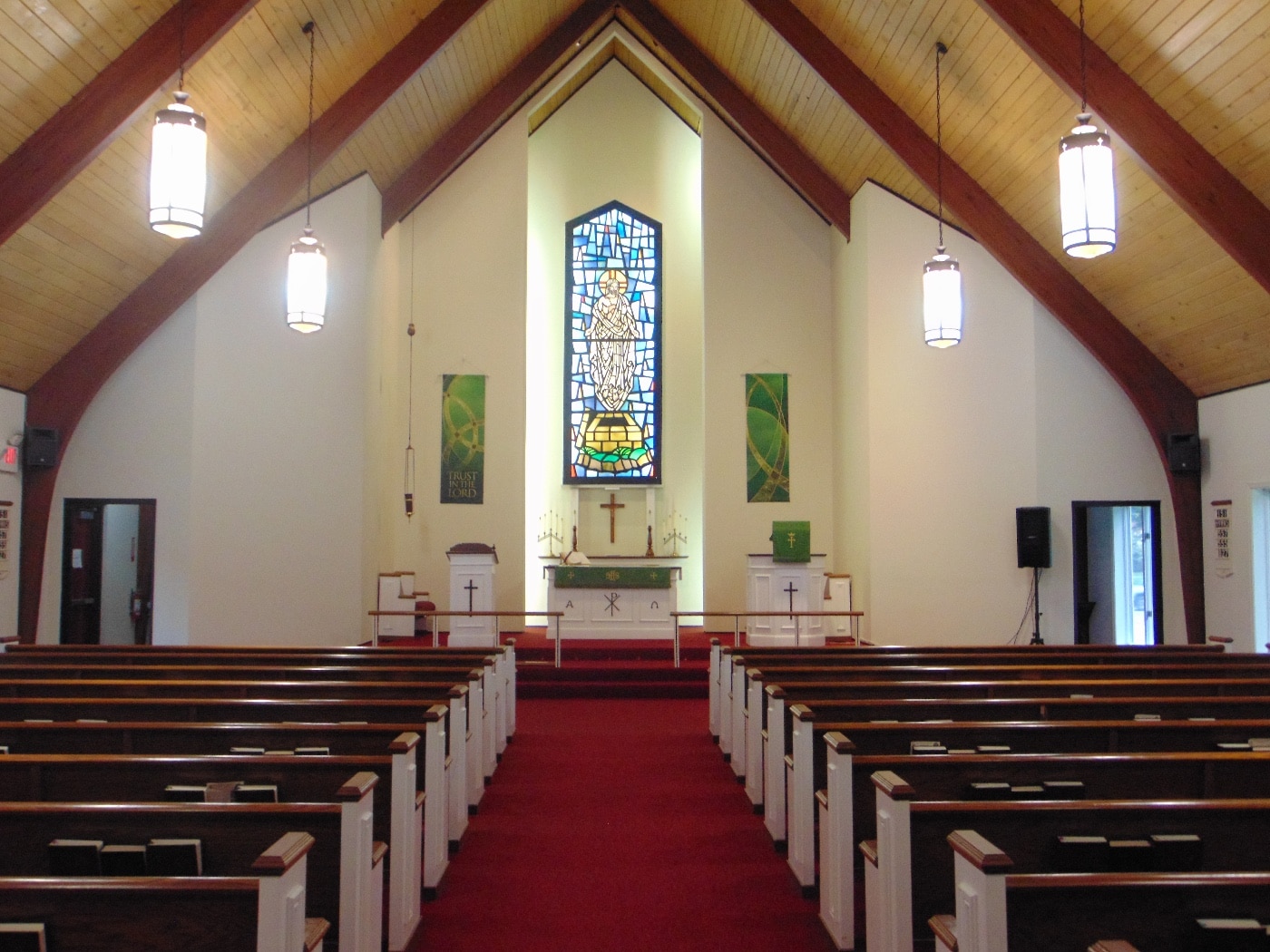 This is a digital photograph of the inside of a church. We can see two exterior doors on either side of the altar in addition to the pews.