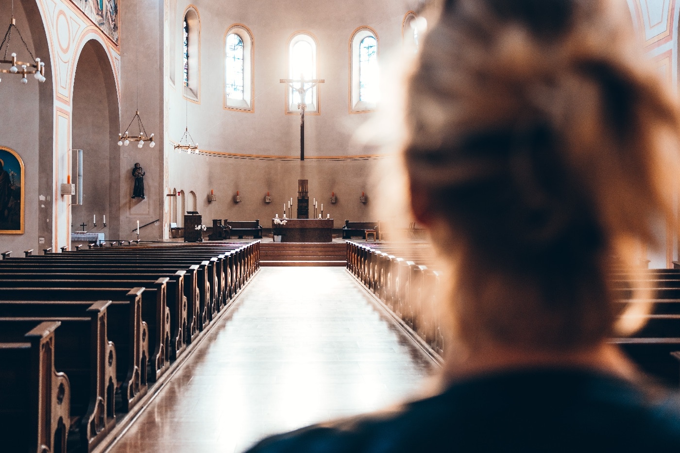 This photo shows us the inside of a large church with a woman in the foreground. Empty pews line both sides of the main walkway. Church security plans should take all of the features into account.