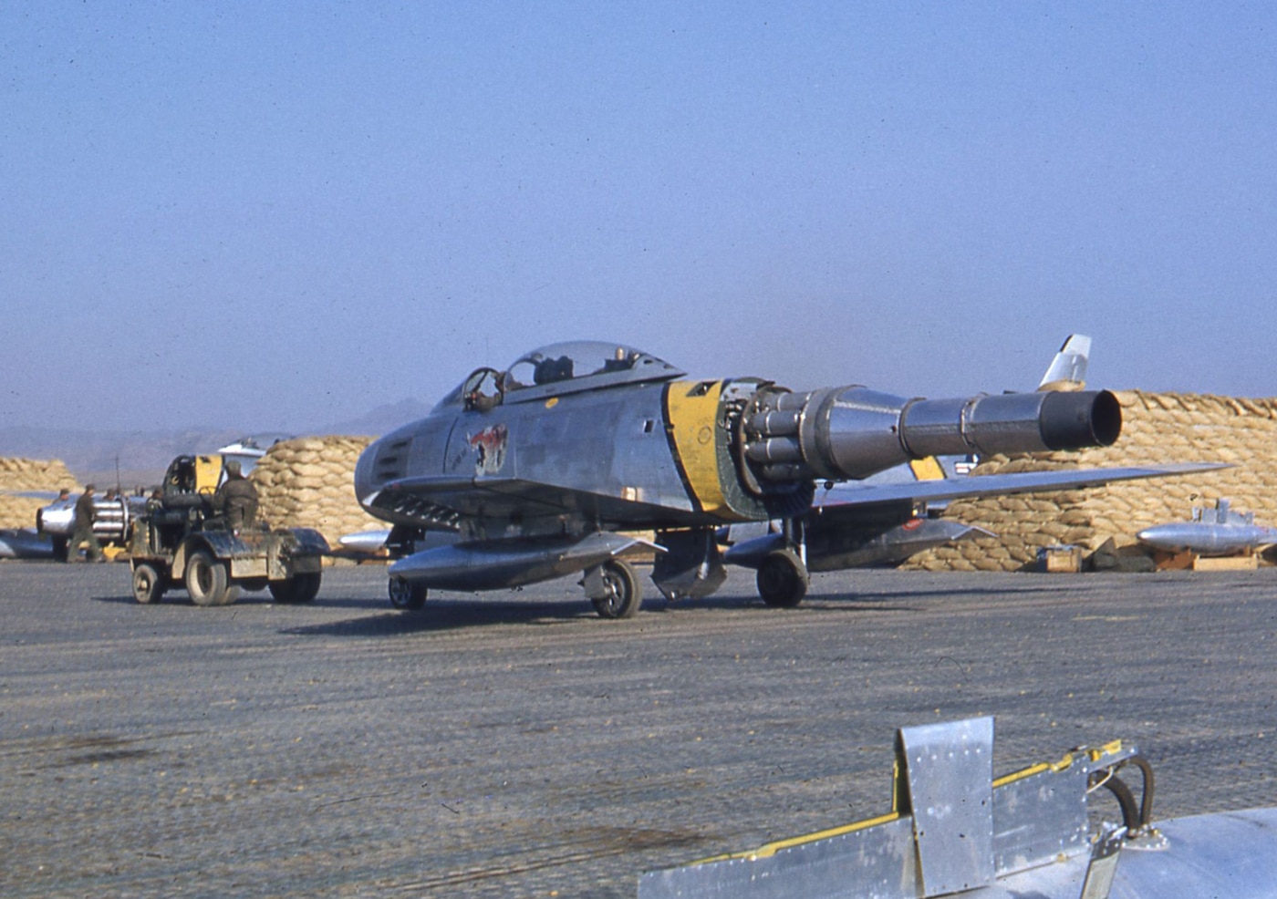 In this image, we see an F-86 that is undergoing repairs. The tail and much of the fuselage was removed to reveal the jet engine. The intake for the engine is in the nose of the plane with the engine running the entire length of the first swept-wing jet fighter. Sabre pilots used this superior thrust to break the speed of sound and set a world speed record with a production model used to achieve this top speed. Although deployed to South Korea, this jet was from Inglewood, California. 