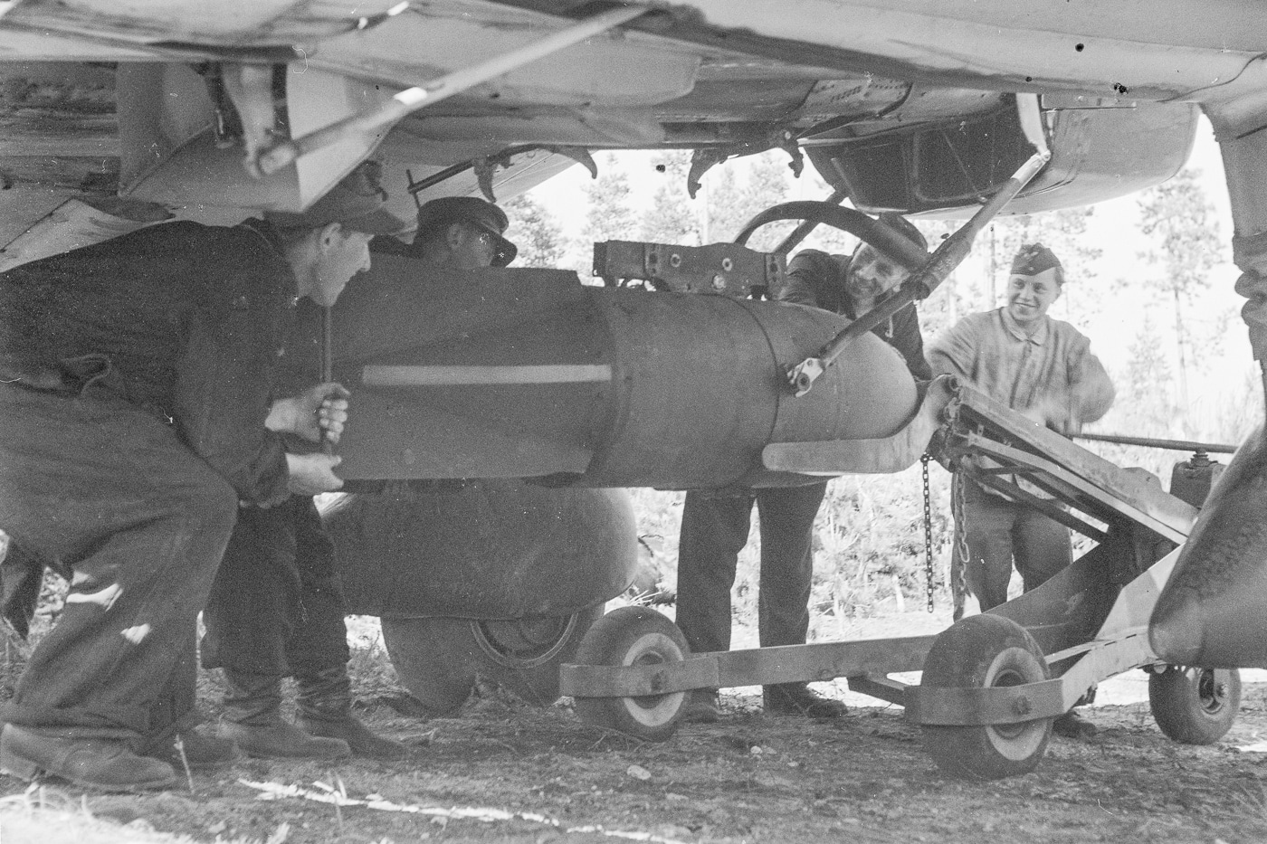 Shown is a 250 kg bomb being lifted onto a Stuka frame hanger using a bomb crane. The bomb is already attached to a "fork" whose function is to prevent the bomb from touching the propeller.